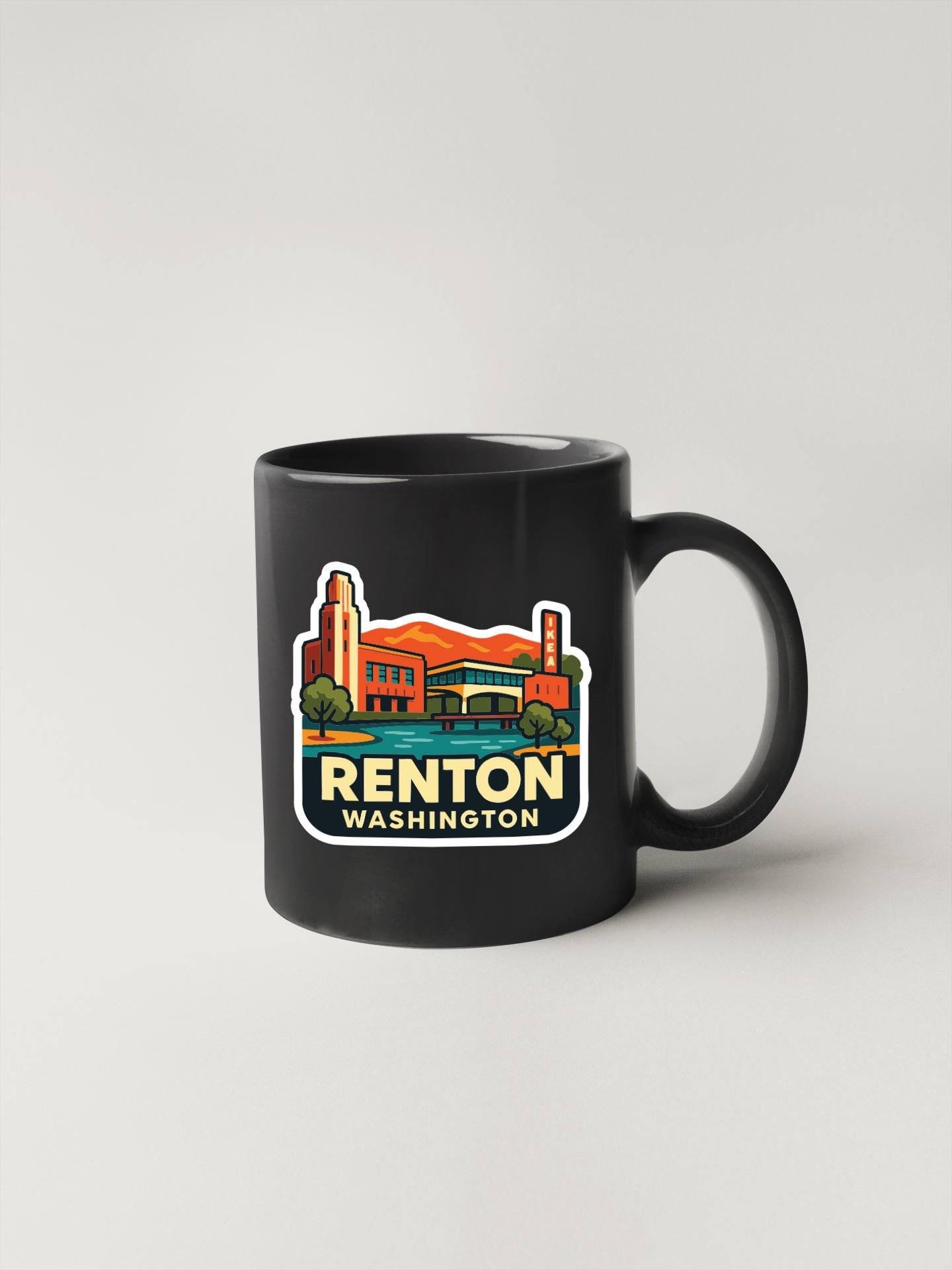 A black coffee mug with a colorful graphic depicting a cityscape and the text "RENTON WASHINGTON" printed on it.