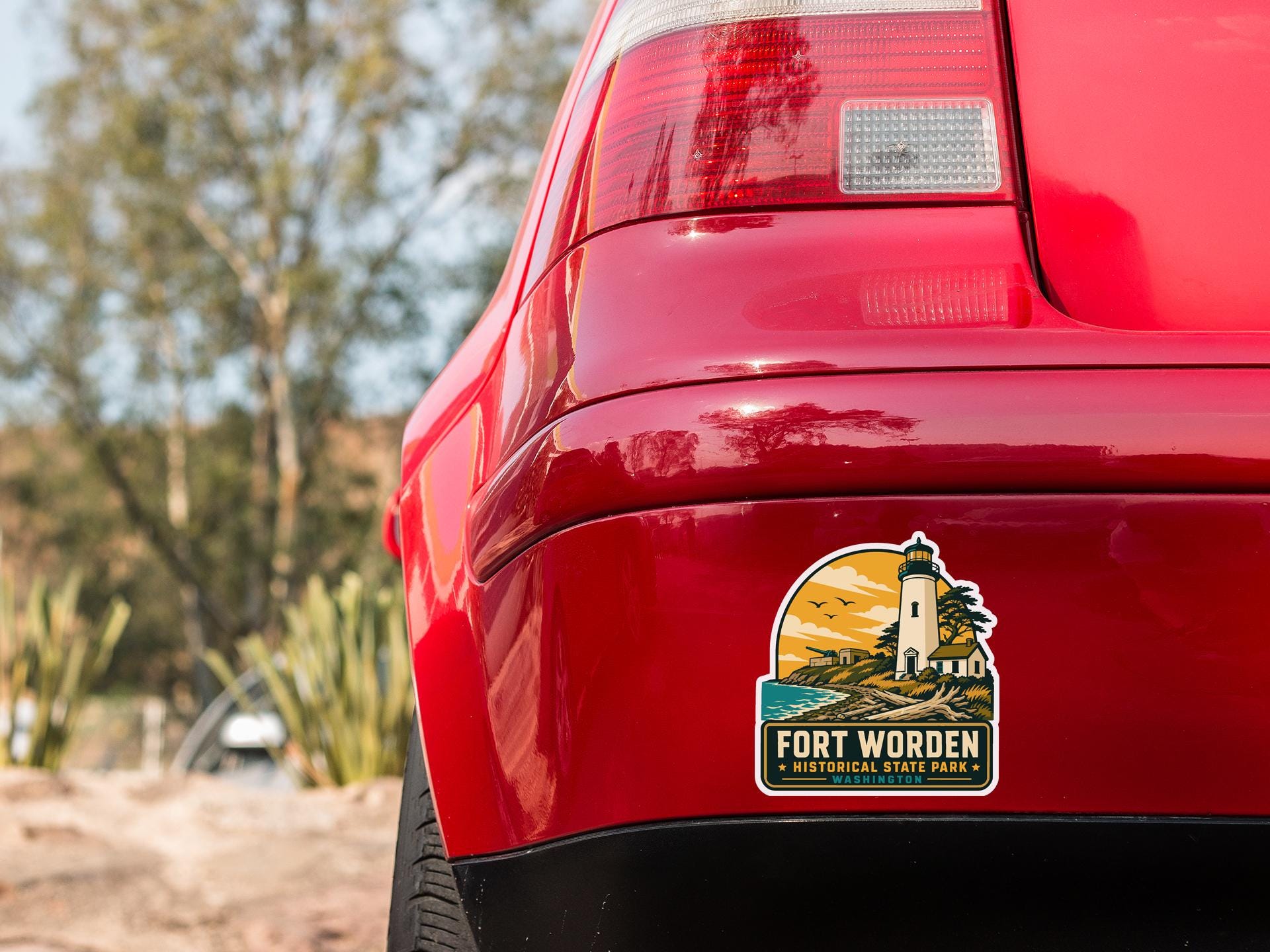 the rear end of a red car with a sticker on the trunk that says "Fort Worden" and "Washington State Lighthouse".