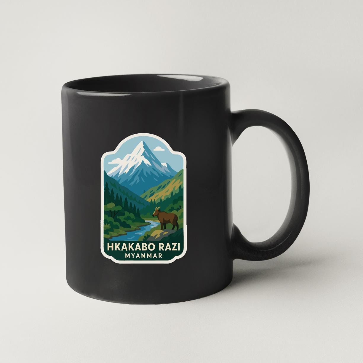 A black coffee mug with a mountain landscape and a brown bear sticker on it.