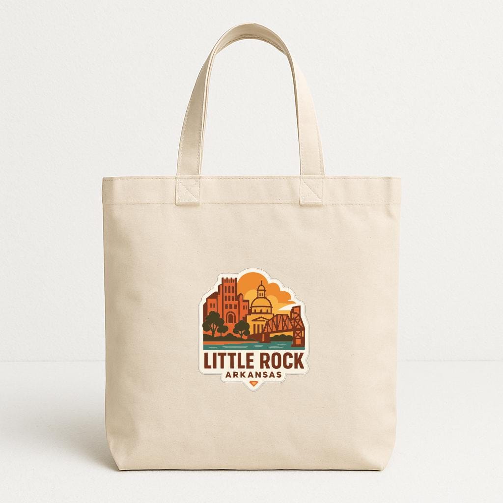 A beige tote bag with a printed design depicting a city skyline and the text "LITTLE ROCK ARKANSAS" on it.