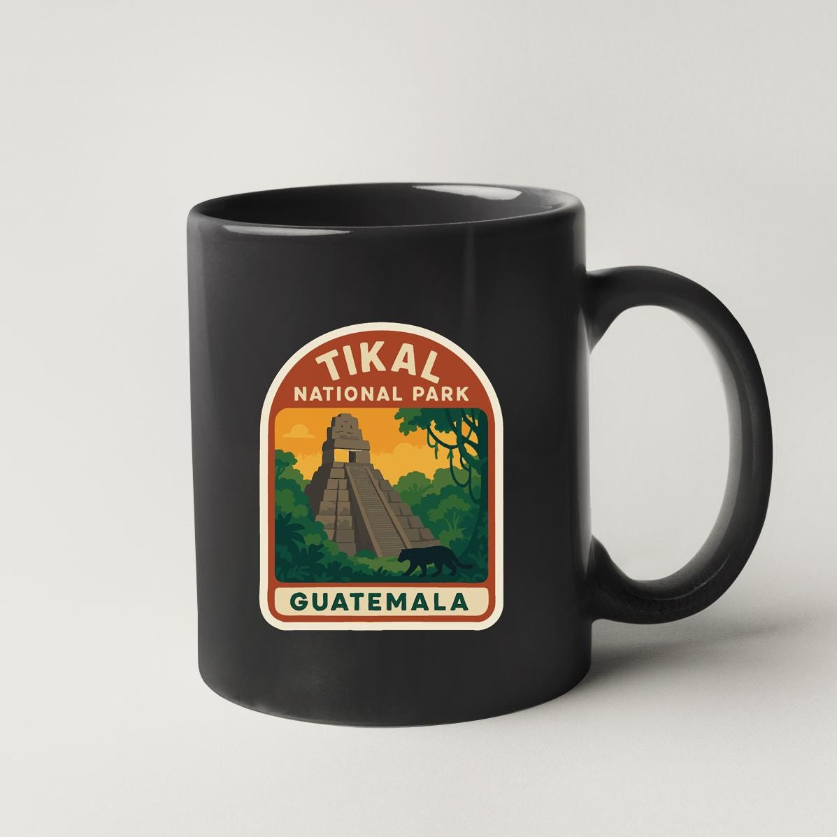 A black coffee mug with a graphic design depicting the Tikal National Park in Guatemala, featuring a pyramid and lush vegetation.