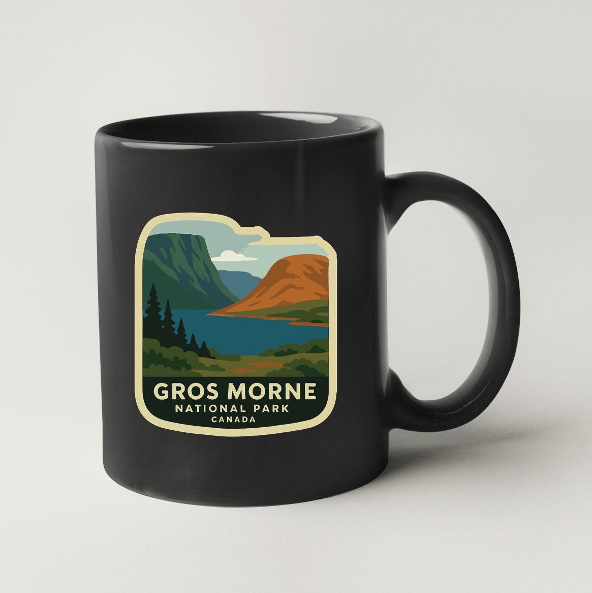 A black coffee mug with a graphic design depicting a scenic landscape featuring mountains, a lake, and trees.