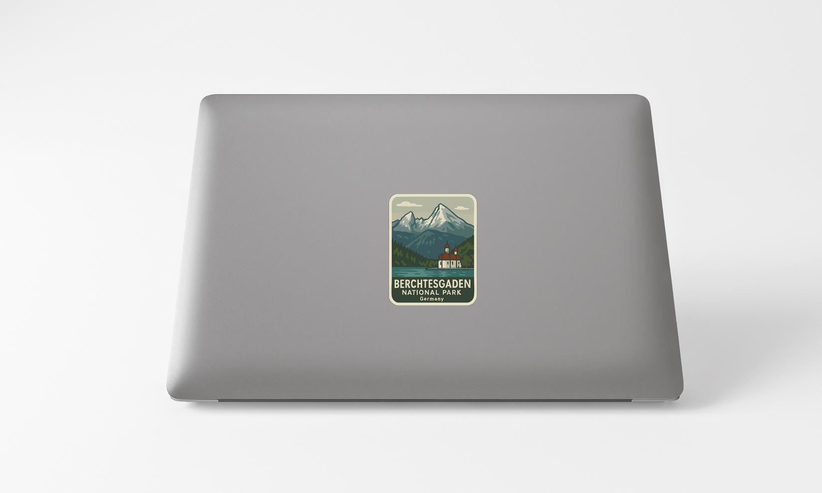 A sticker on the back of a laptop, depicting a mountain landscape with a small building in the center.