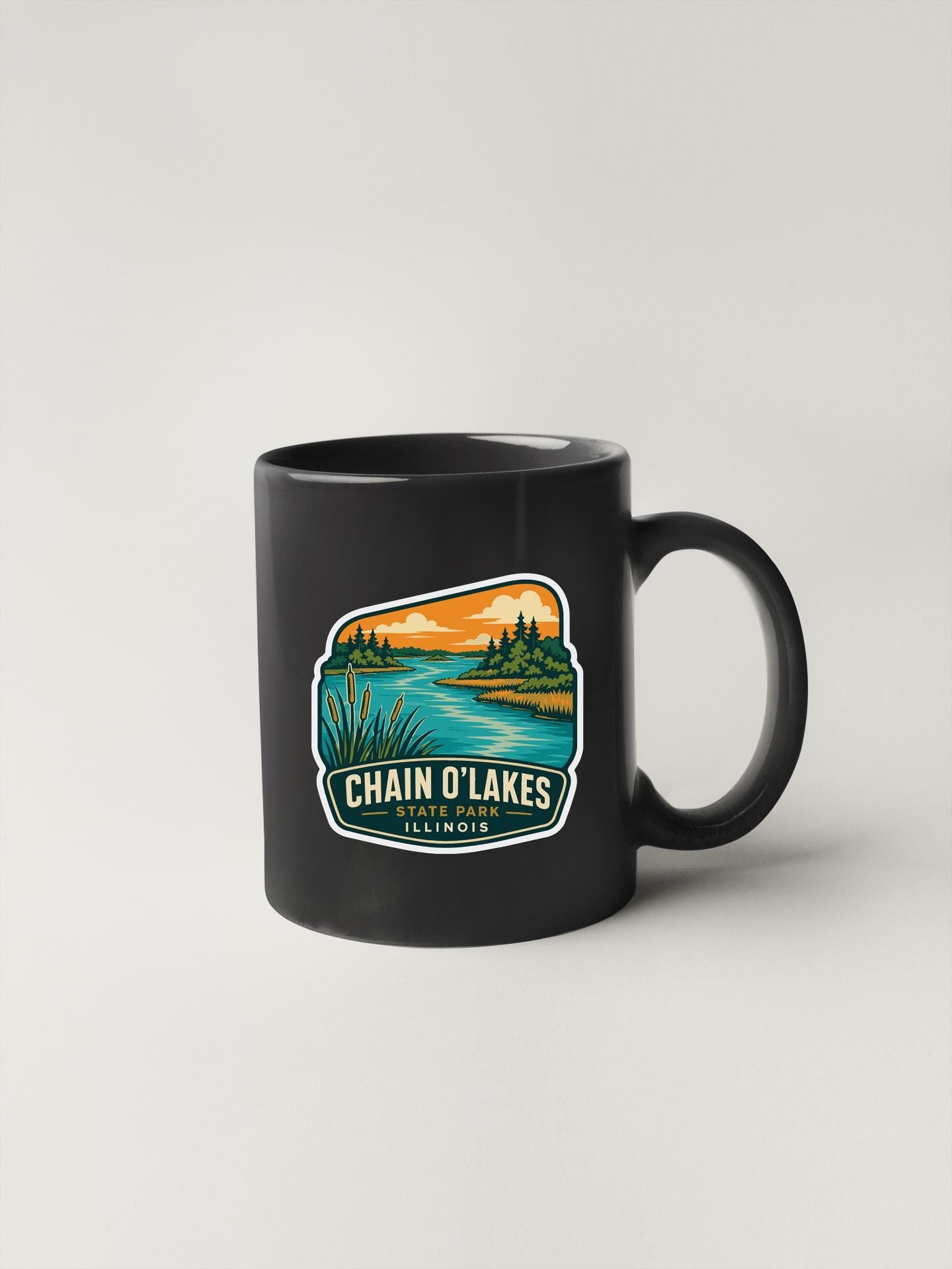 A black coffee mug with a colorful graphic depicting a scenic lake landscape.