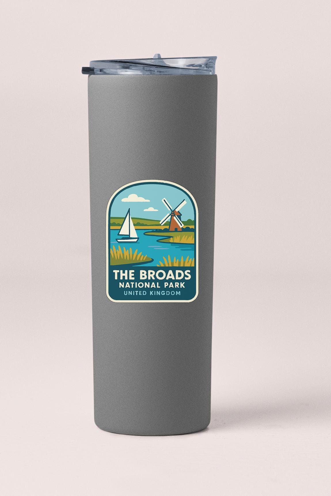 A gray insulated tumbler with a label that features an illustration of a sailboat and a windmill, along with the text "THE BROADS NATIONAL PARK UNITED KINGDOM".