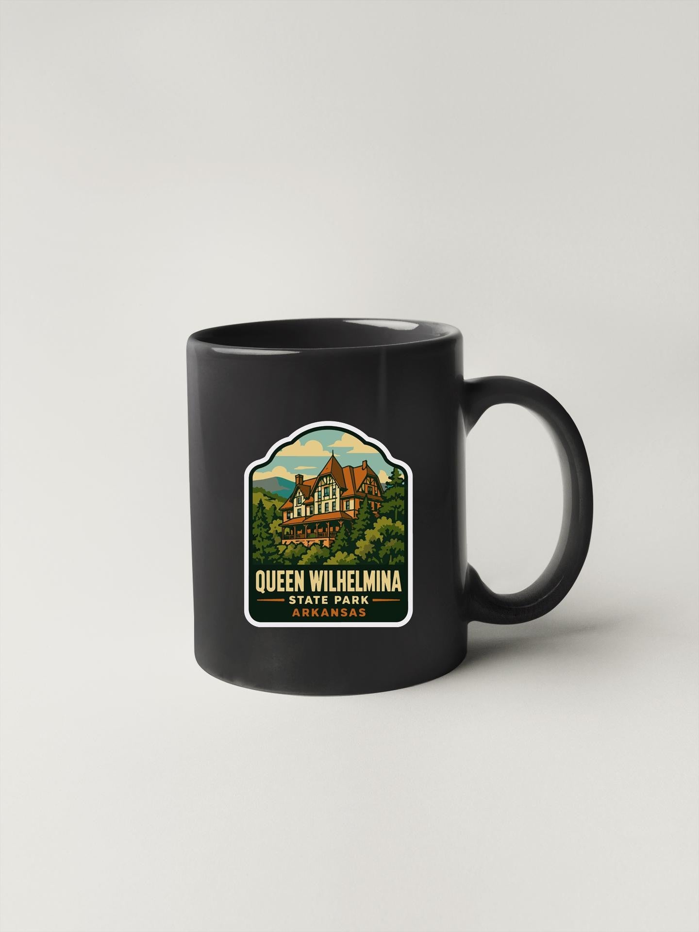 A black coffee mug with a sticker depicting Queen Wilhelmina State Park in Arkansas.