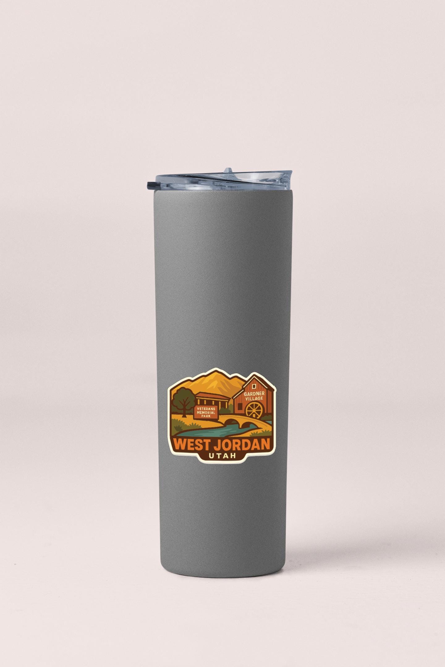 A gray insulated tumbler with a sticker depicting a scenic landscape and the text "WEST JORDAN UTA".