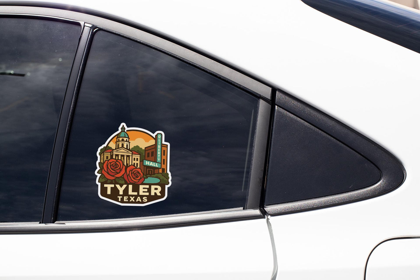 A sticker on the side of a car window, featuring a colorful illustration of a city skyline with a prominent building labeled " Tyler, Texas".