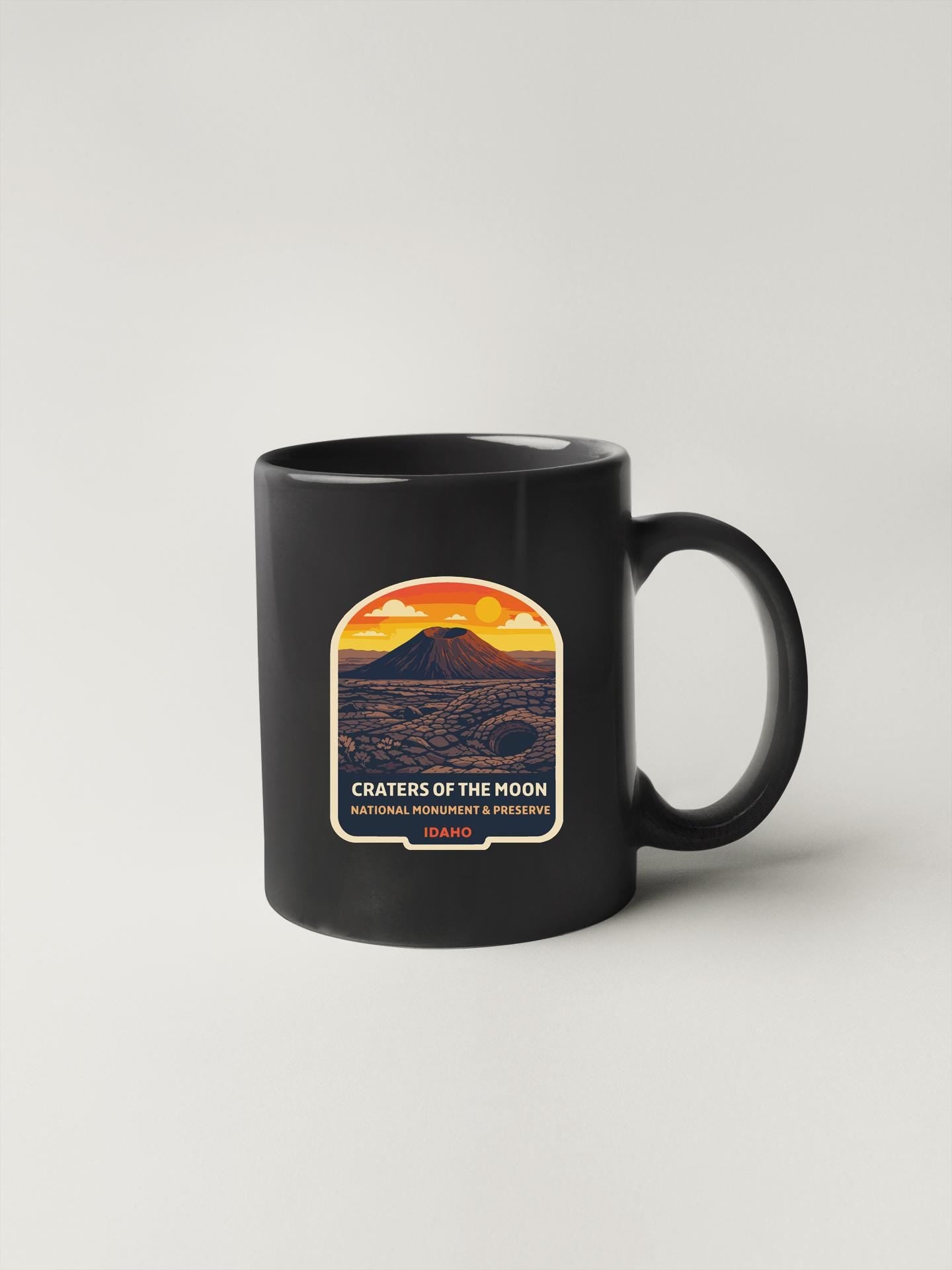 A black coffee mug with a graphic design depicting Craters of the Moon National Monument & Preserve.