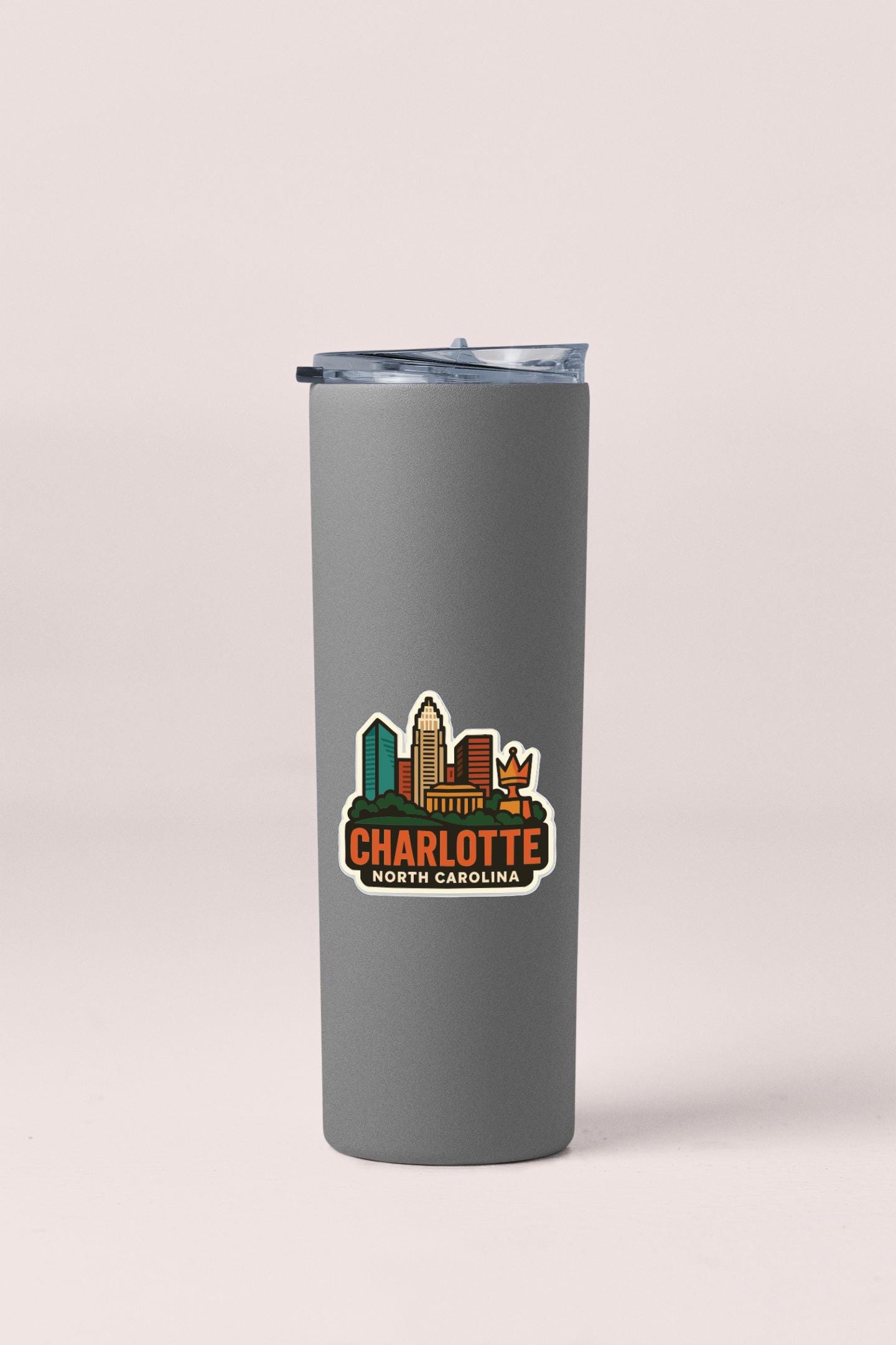 A gray insulated tumbler with a printed sticker depicting the skyline of Charlotte, North Carolina.