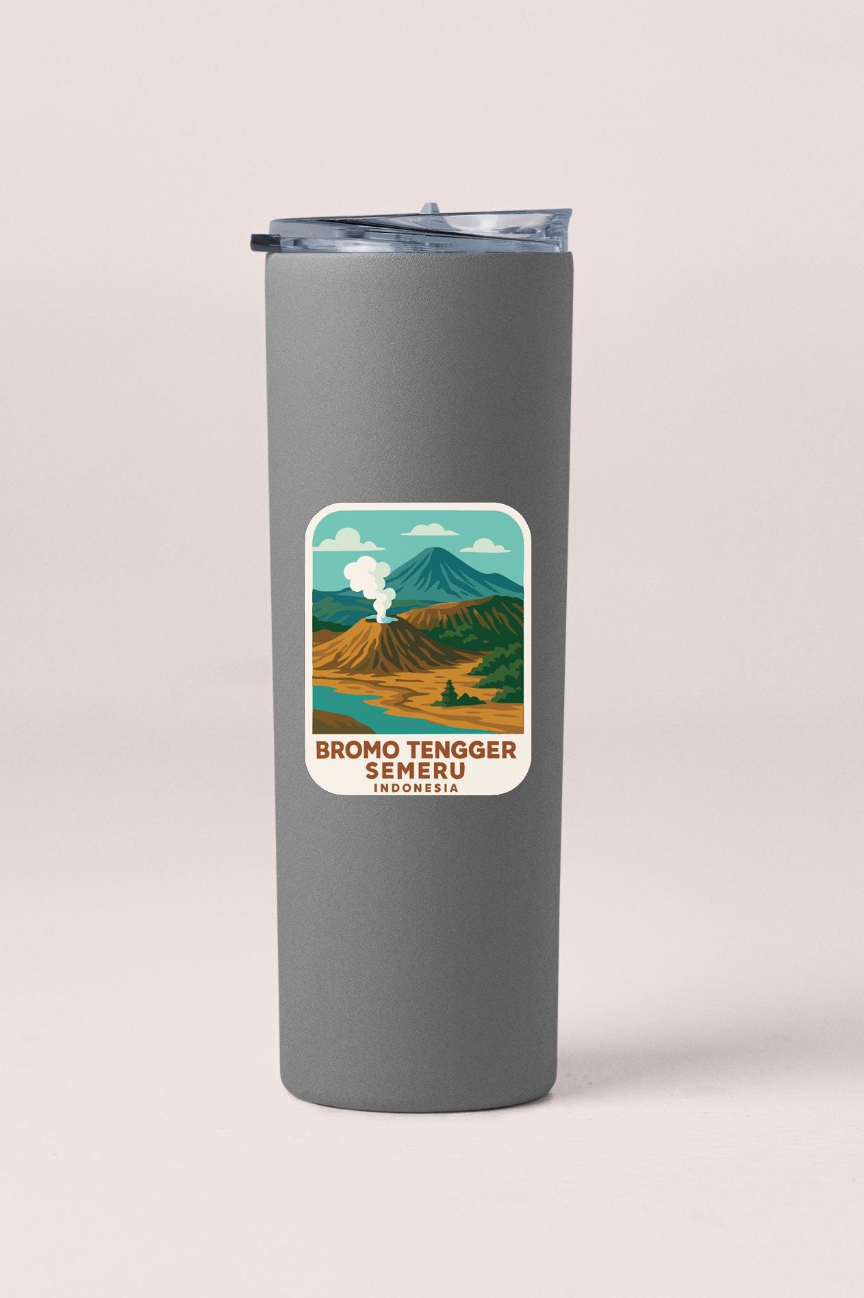 A gray insulated tumbler with a label that features an illustration of a mountain range and a steam-like figure, along with the text "BROMO TENGGER SEMERU INDONESIA".