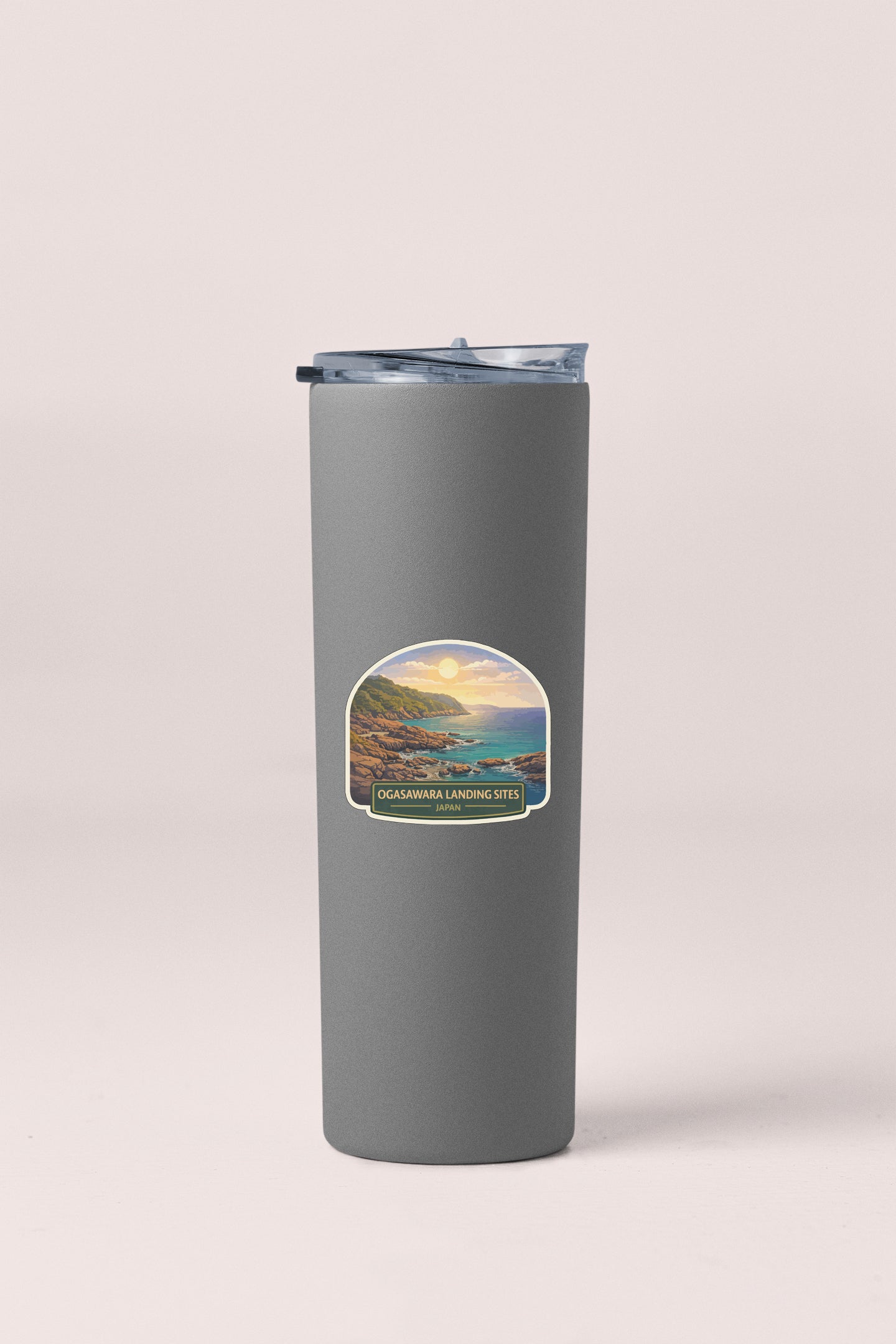A gray insulated tumbler with a lid and a sticker depicting a scenic coastal landscape.