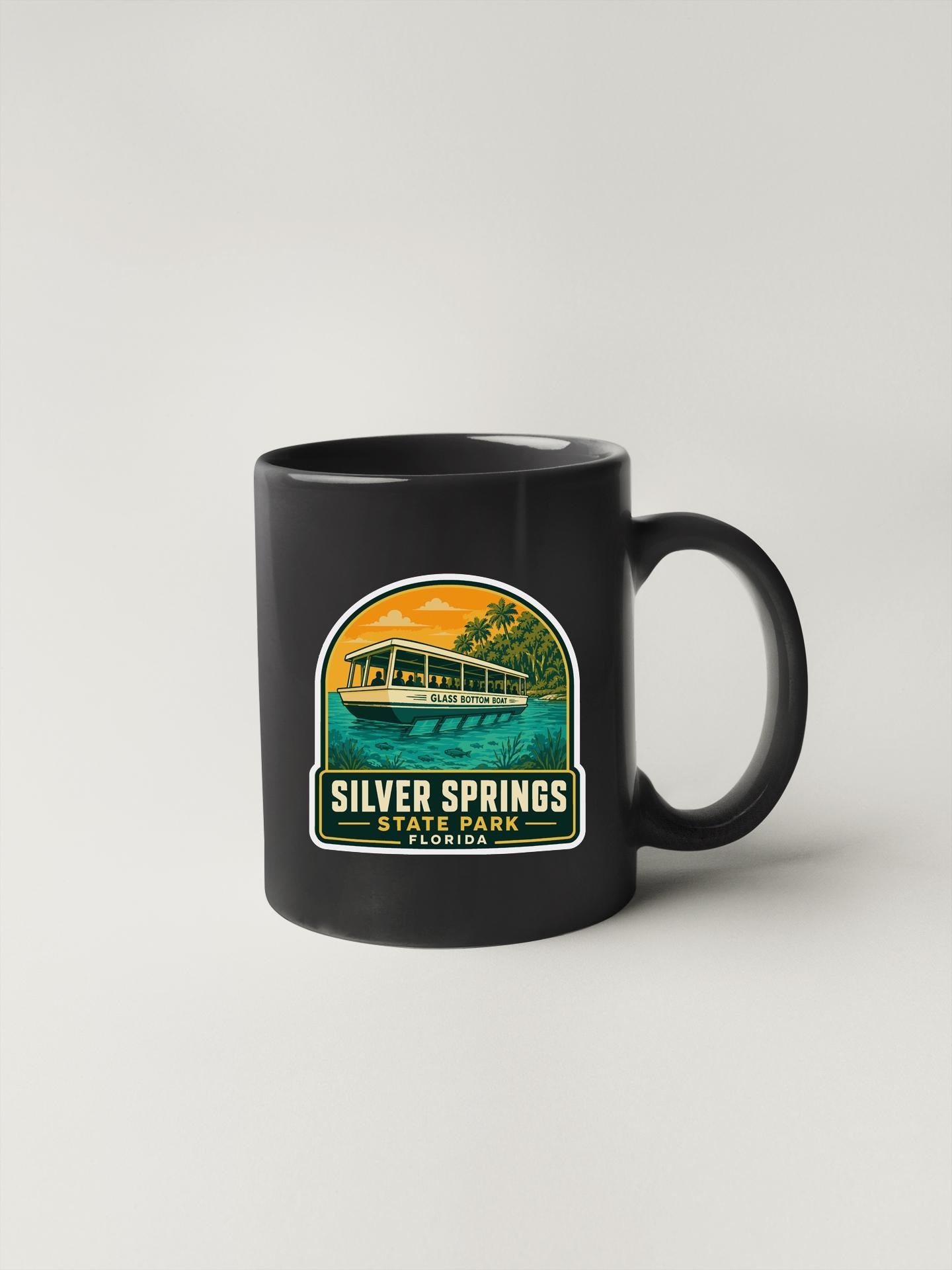 A black coffee mug with a graphic design depicting a boat on a lake, surrounded by palm trees and a sunset.