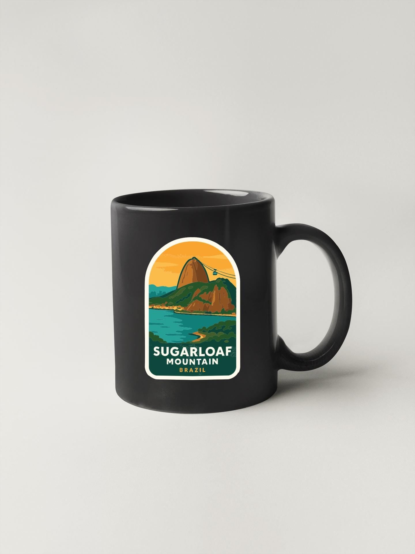 A black coffee mug with a graphic design depicting Sugarloaf Mountain in Brazil.