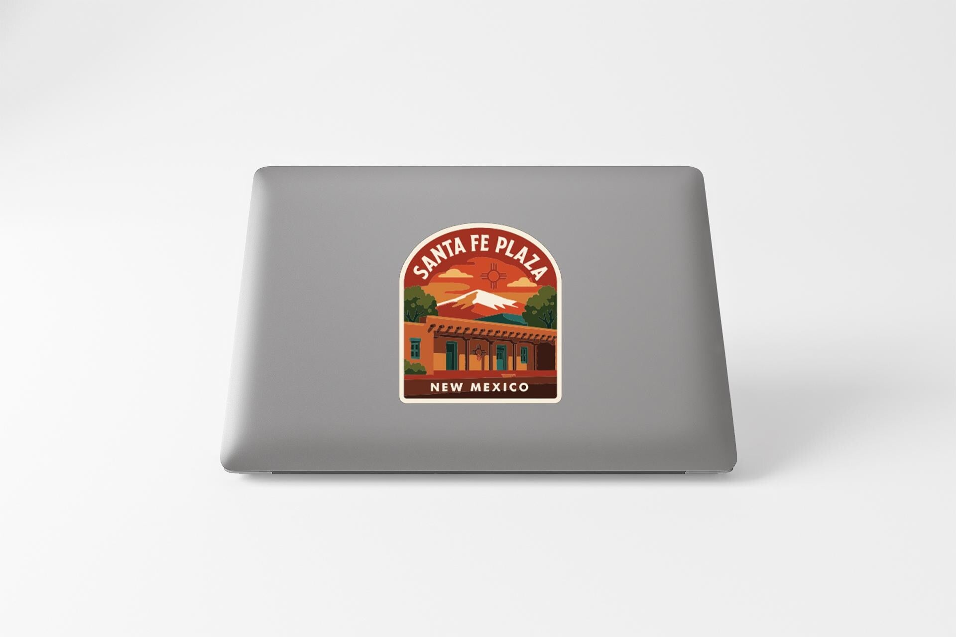 A sticker on the back of a laptop that features an illustration of Santa Fe Plaza, a famous landmark in New Mexico.