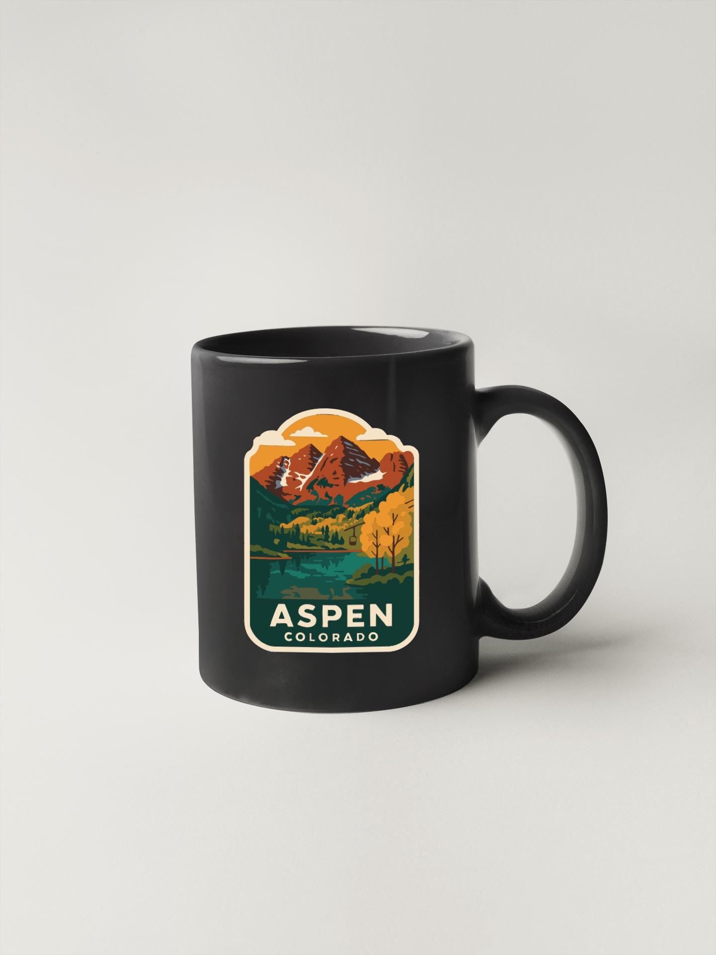 A black coffee mug with a colorful graphic depicting a mountain landscape and the text "Aspen, Colorado" printed on it.