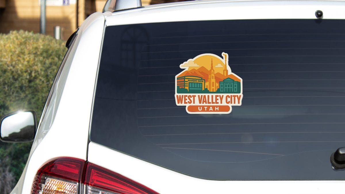 A sticker on the rear window of a white vehicle, depicting a cityscape with mountains in the background.