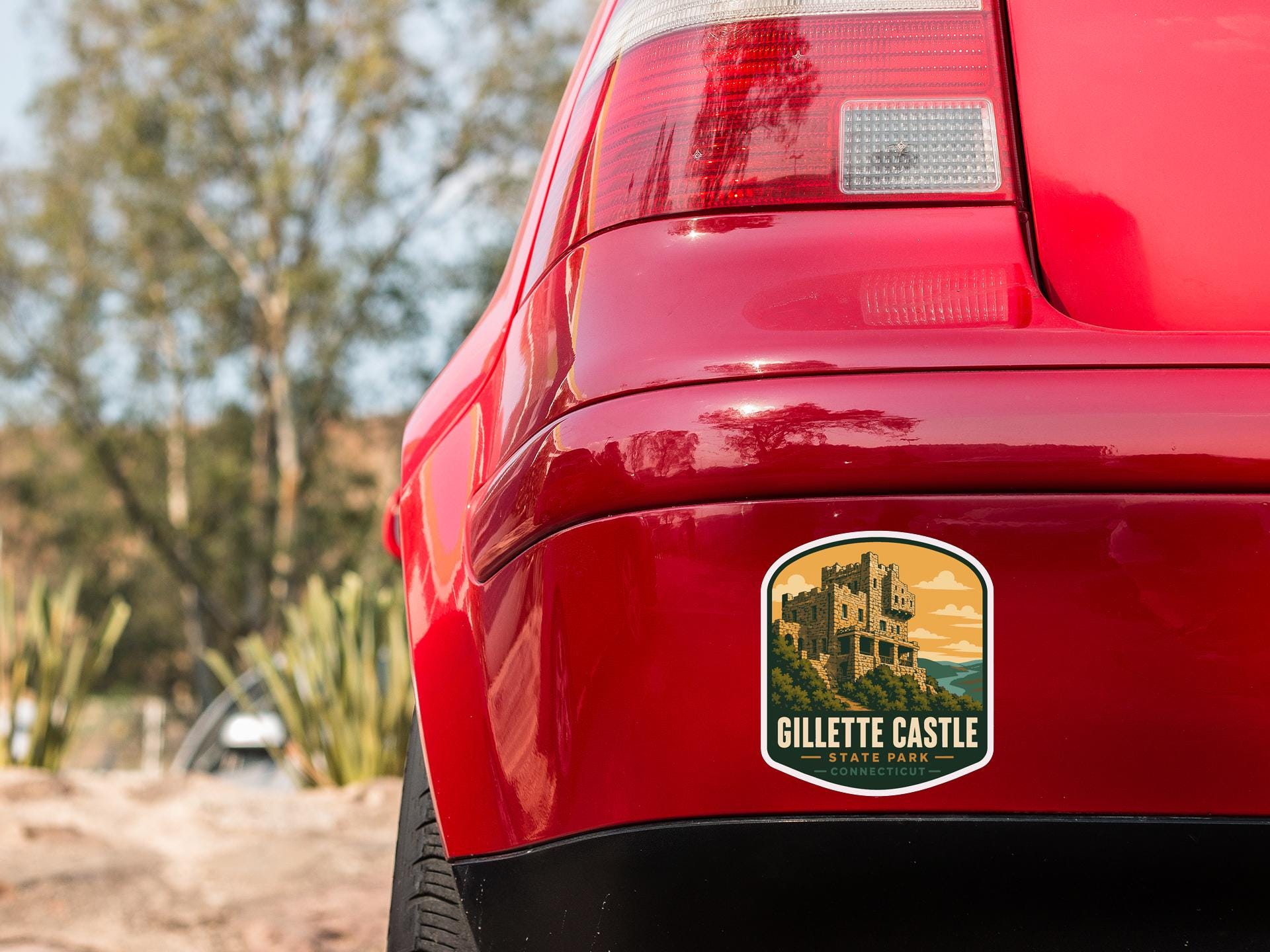 the rear end of a red car with a sticker on the trunk that reads "GILLETTE CASTLE STATE PARK".