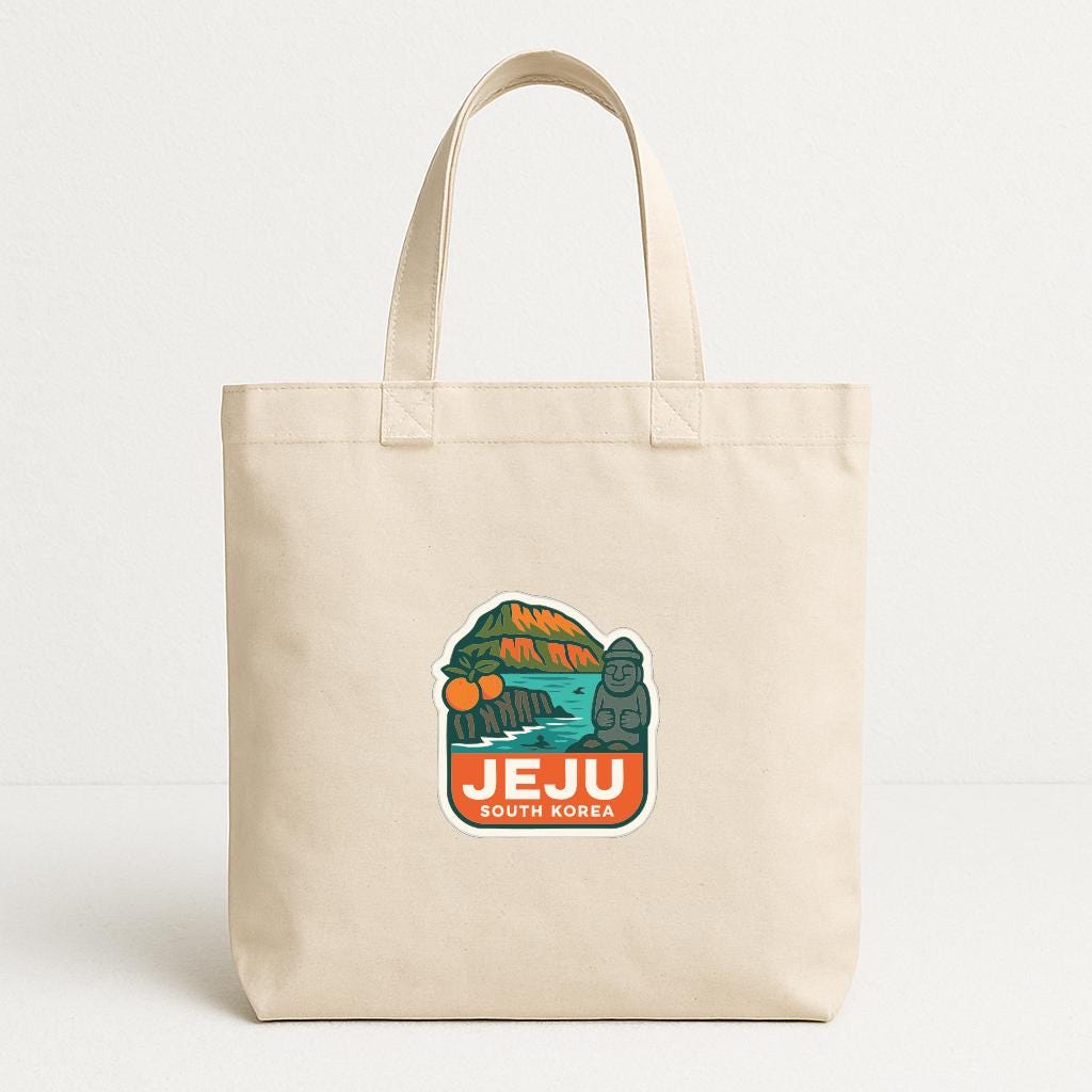 A beige tote bag with a graphic design featuring a mountain, palm trees, and the text "JEJU SOUTH KOREA".