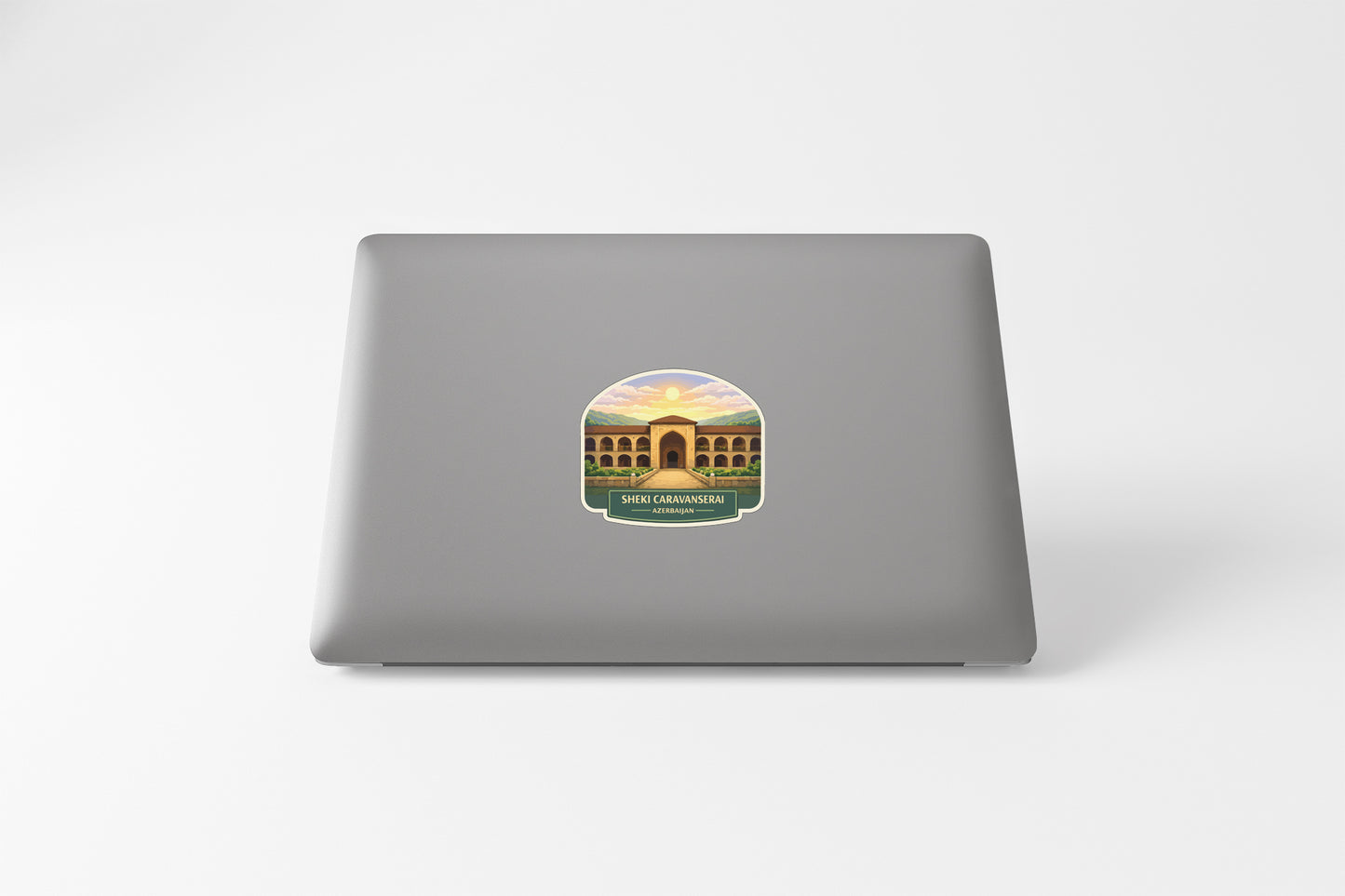 A sticker depicting a building with arches and a sunset in the background is placed on the back of a laptop.