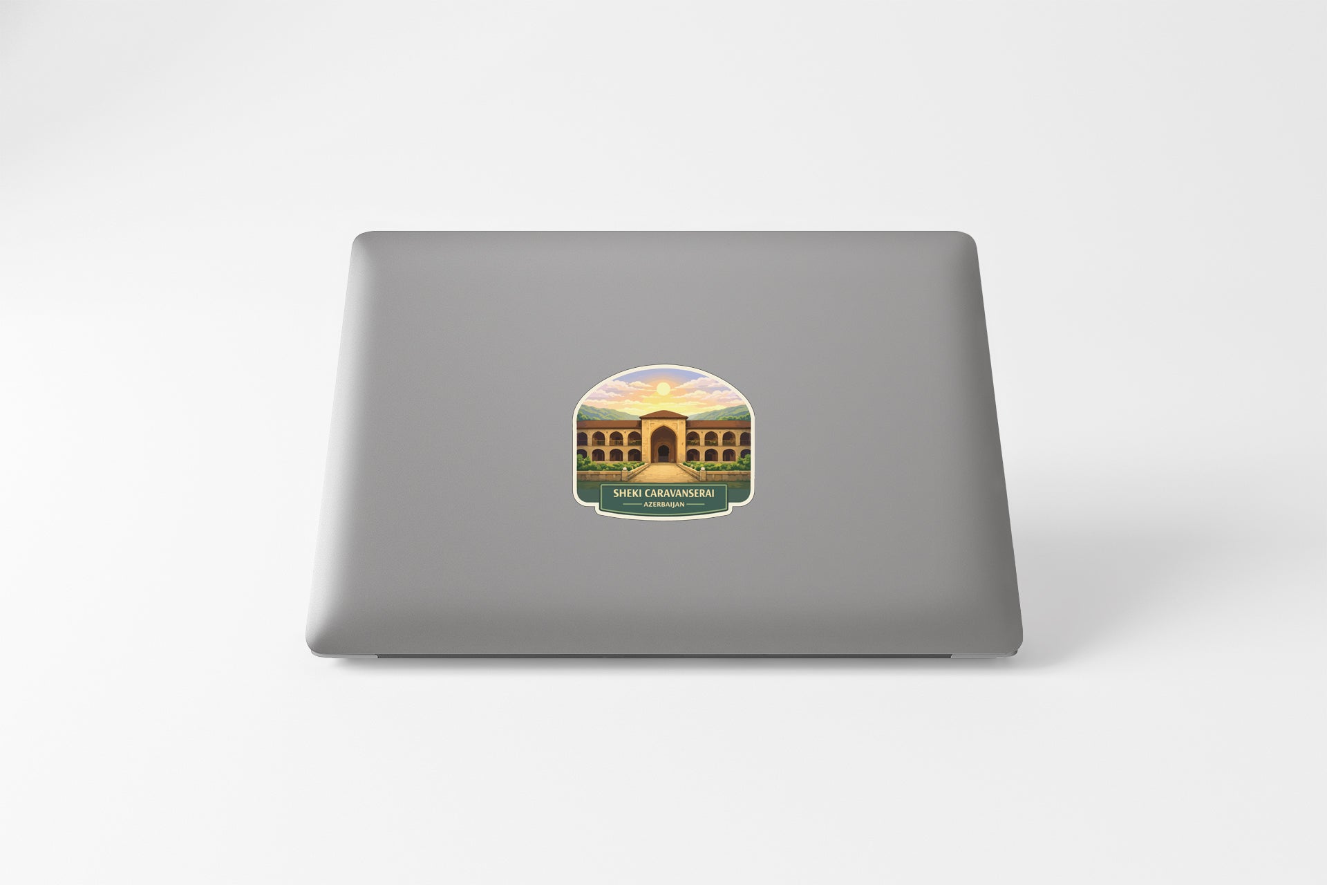 A sticker depicting a building with arches and a sunset in the background is placed on the back of a laptop.