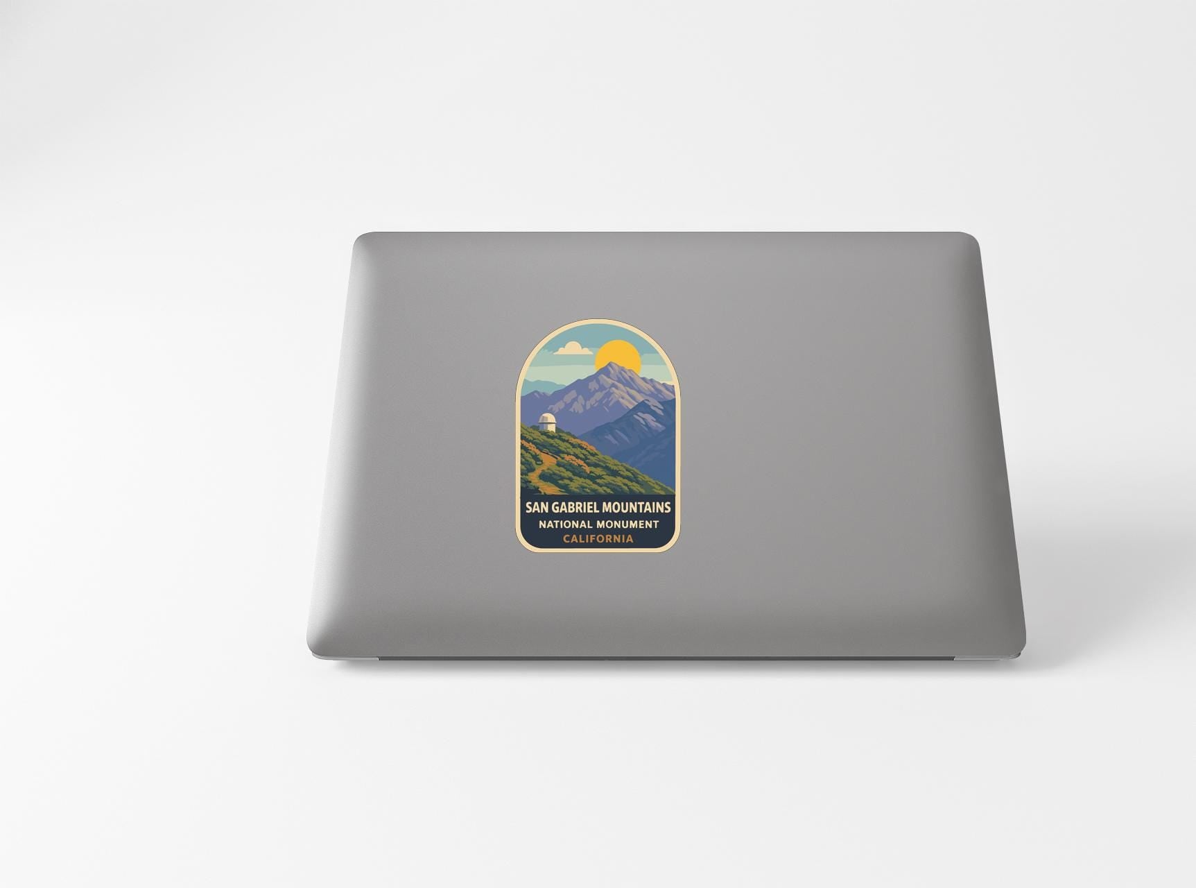 a sticker with a mountain landscape and a sun, placed on the back of a laptop.