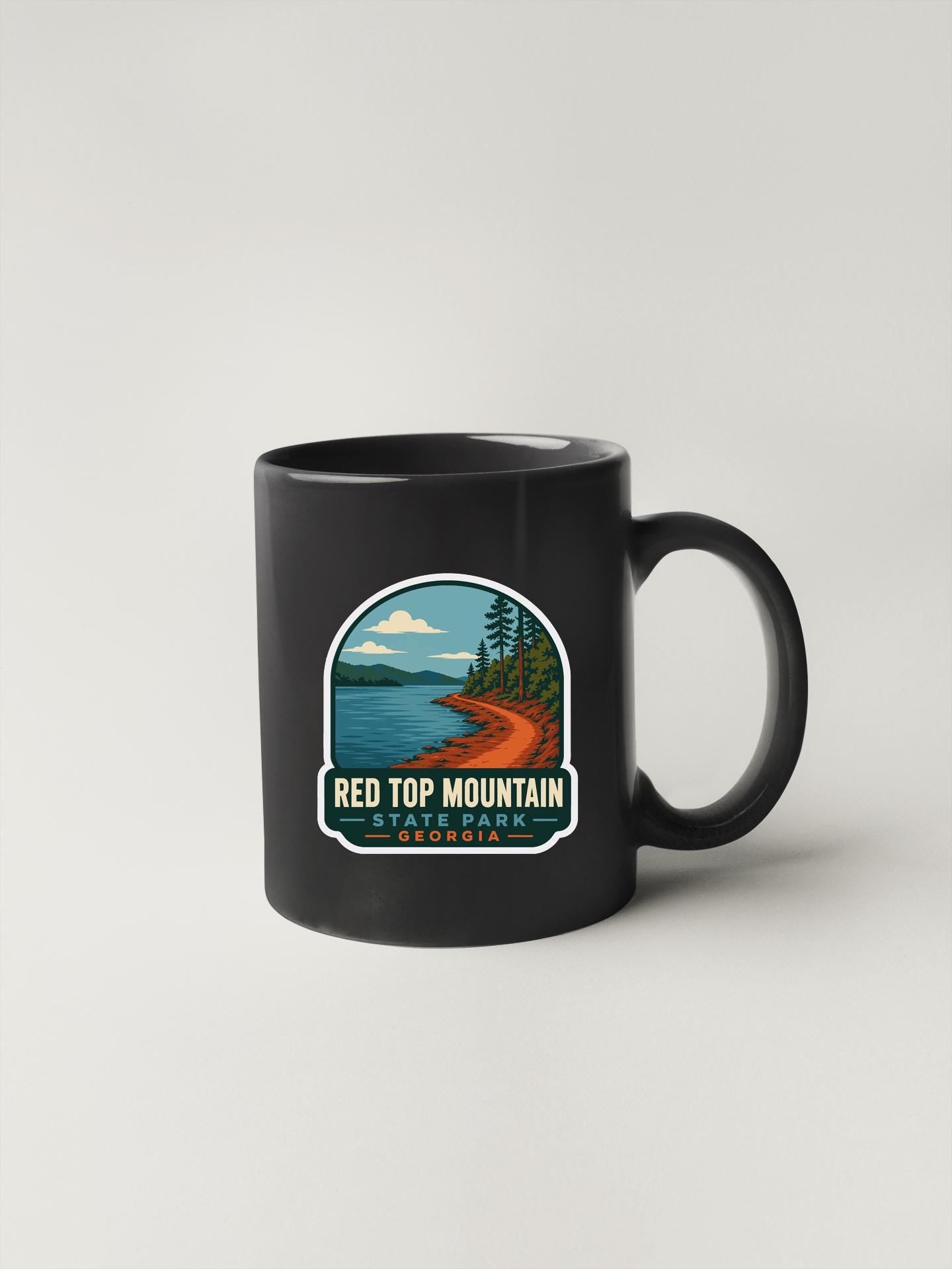 A black coffee mug with a graphic design depicting a scenic mountain landscape with a lake and pine trees.