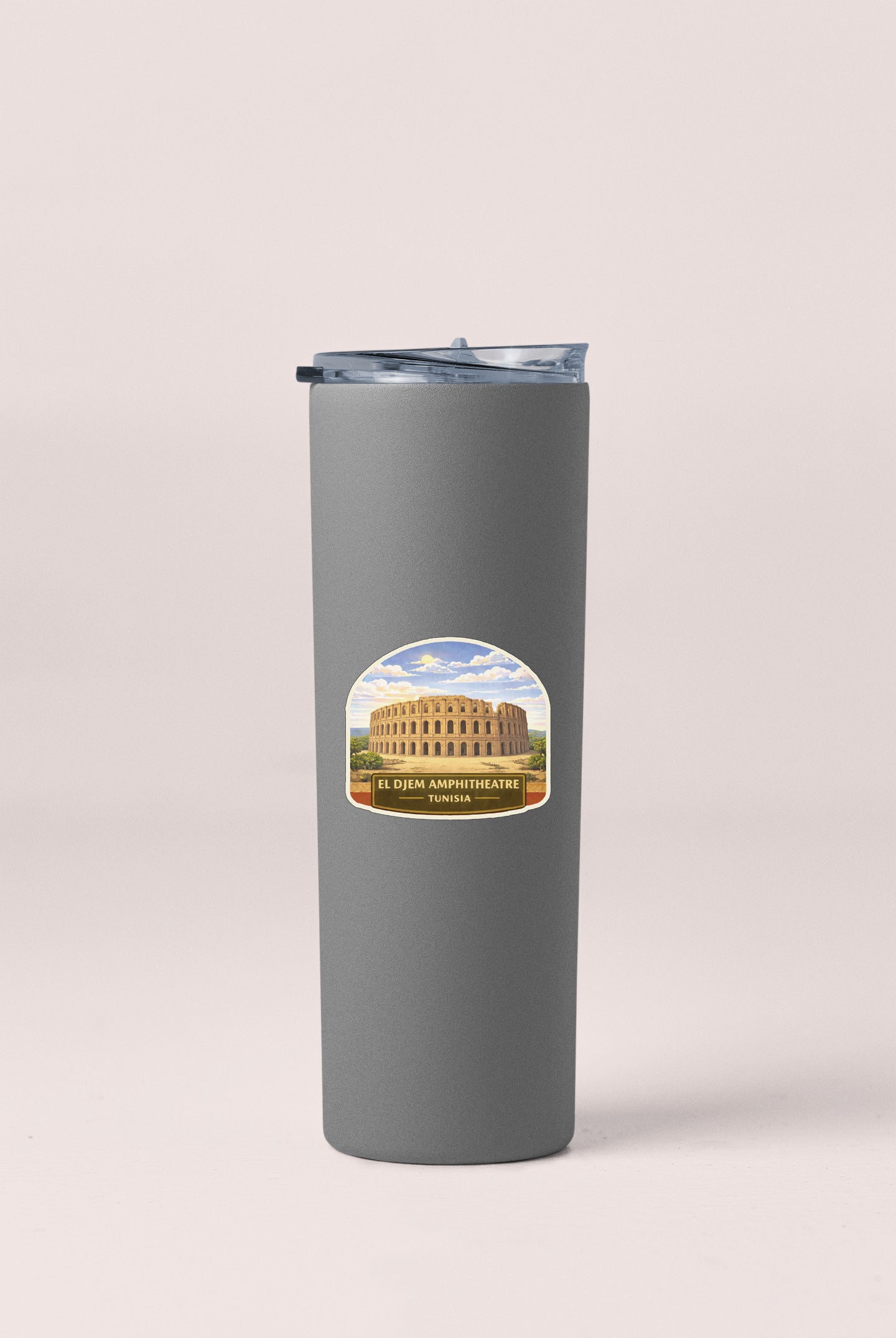 A gray insulated tumbler with a label featuring an illustration of the El Comé Amphitheatre in Tunis.