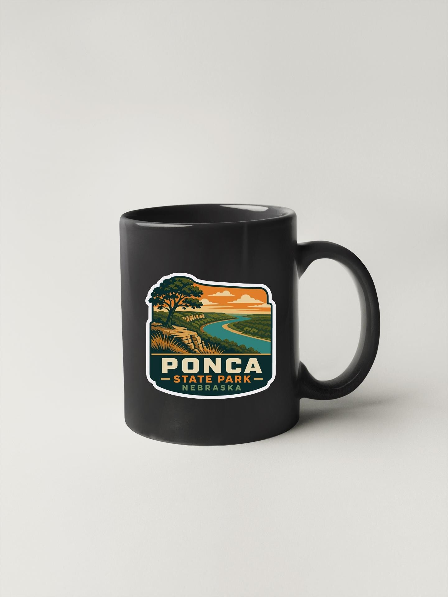 A black coffee mug with a graphic design depicting a scenic landscape, including a river, mountains, and a sunset.