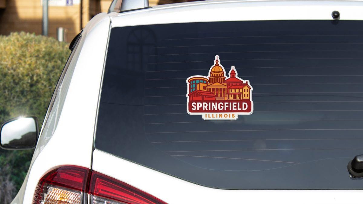 A sticker on the rear window of a white vehicle, depicting a city skyline with the text "Springfield Illinois".