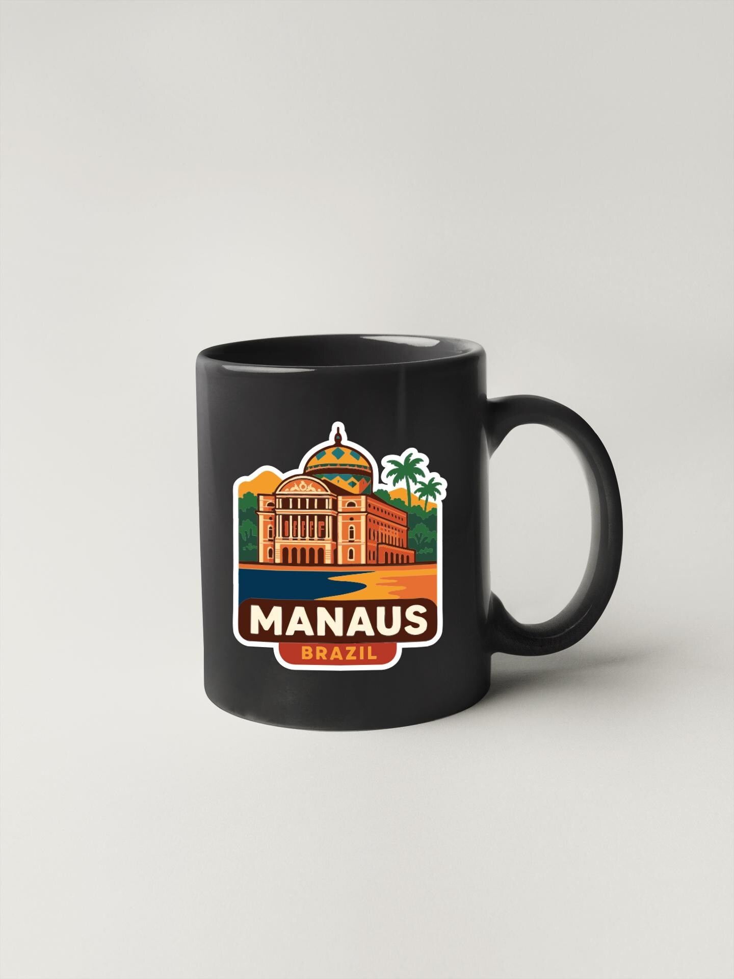 A black coffee mug with a colorful sticker depicting the Manaus, Brazil, featuring a building and palm trees.