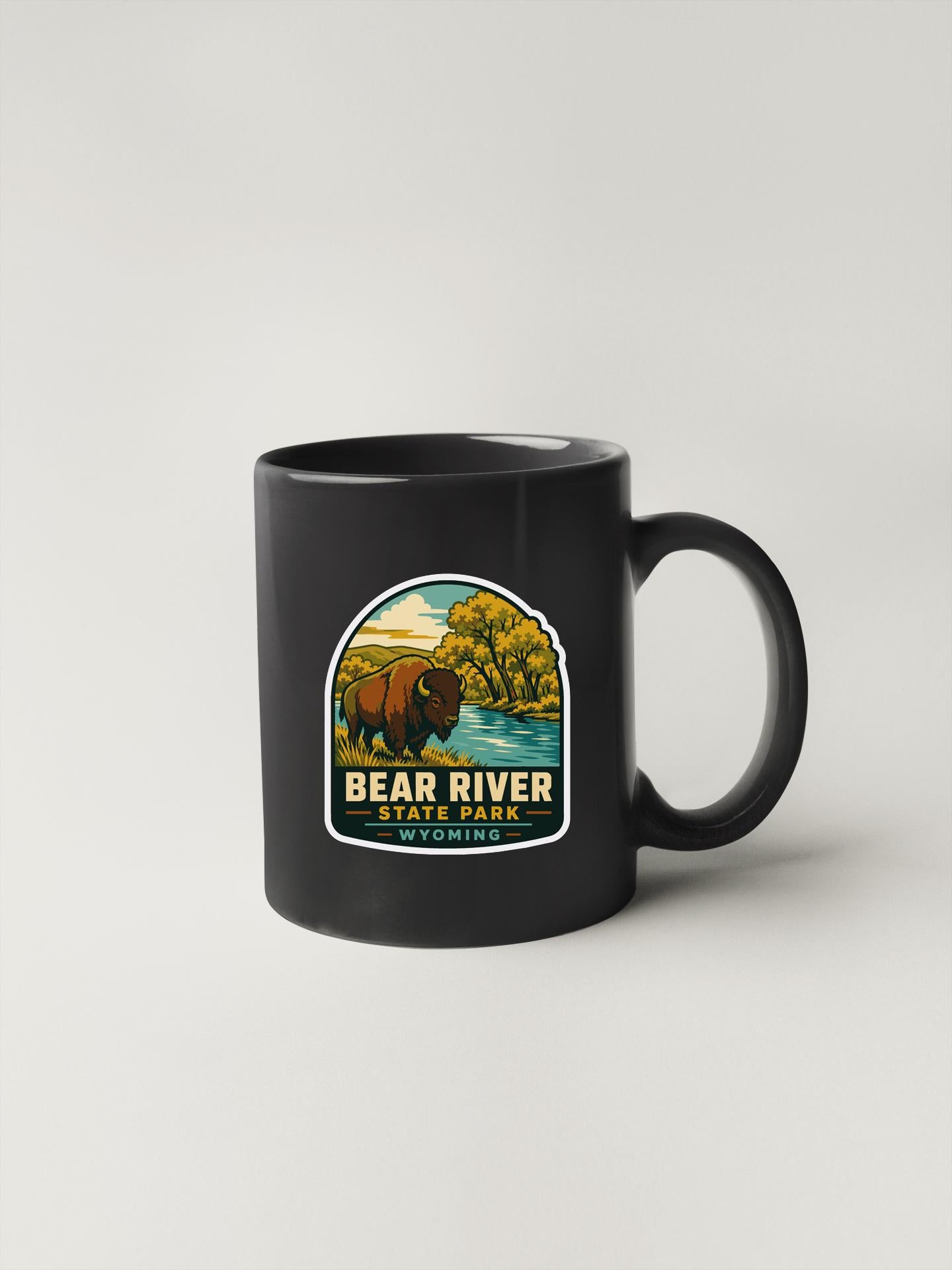 A black coffee mug with a sticker depicting a bison in a scenic landscape, along with the text "BEAR RIVER STATE PARK" printed on it.