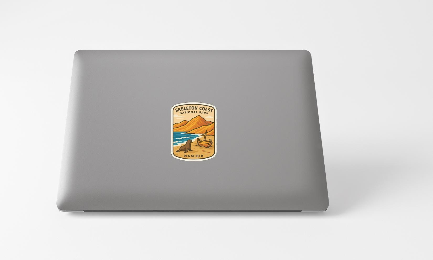 A sticker on the back of a laptop, depicting a scenic landscape with mountains, a beach, and a body of water.