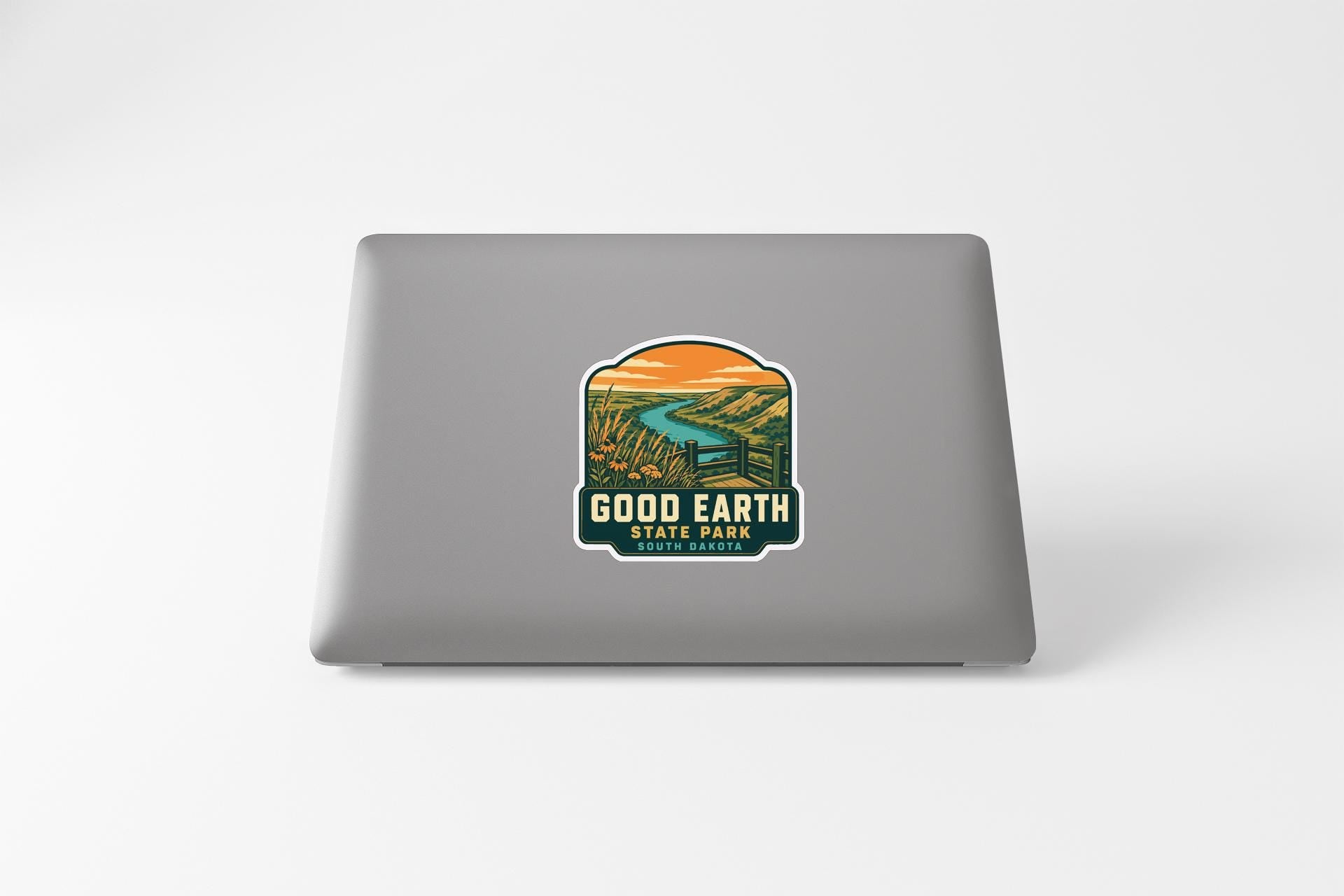 A sticker on the back of a laptop, depicting a scenic landscape with a river and mountains.