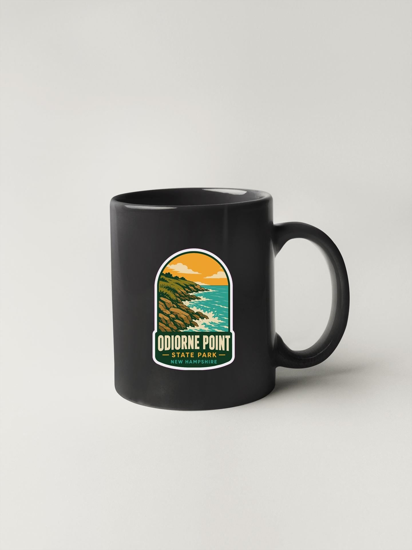 A black coffee mug with a sticker depicting a scenic landscape, specifically Odierne Point State Park.