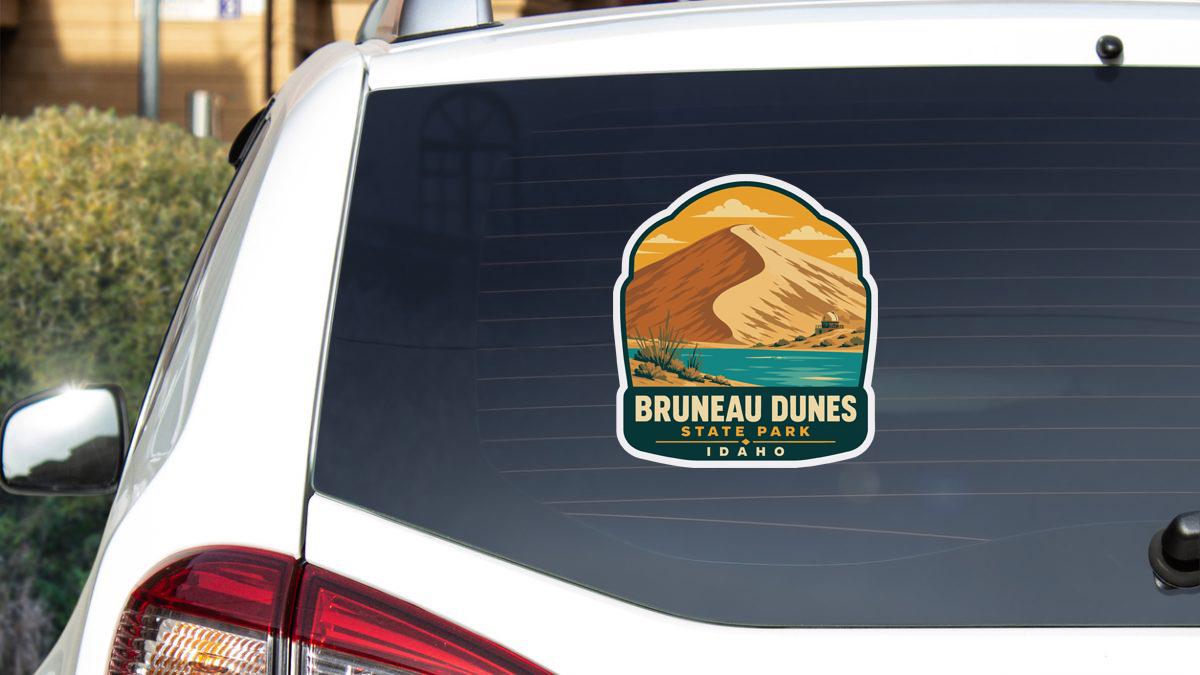 A sticker on the rear window of a white car, depicting a scenic landscape with mountains and a body of water.