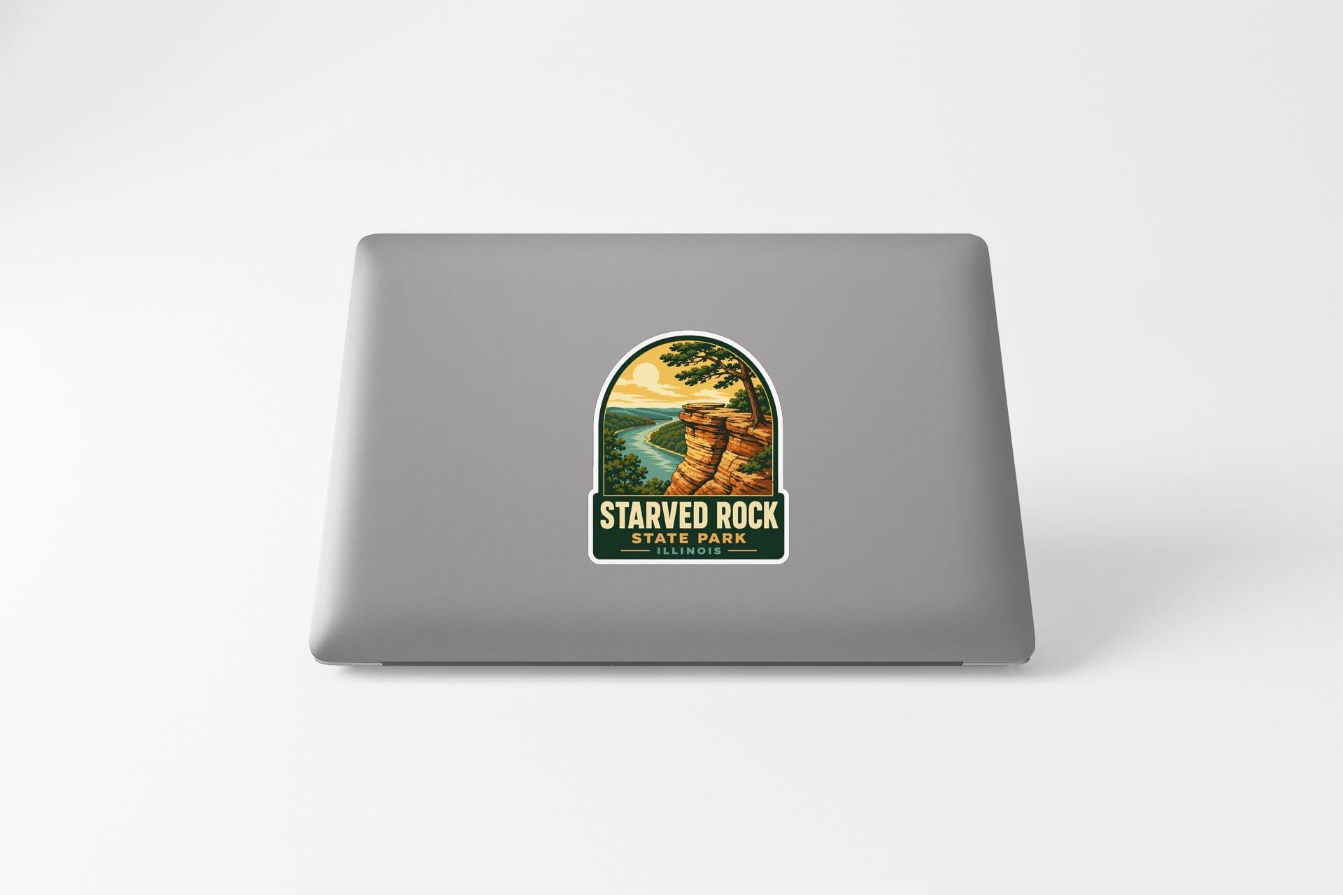 A sticker on the back of a laptop, depicting a scenic landscape with a cliff and a river.