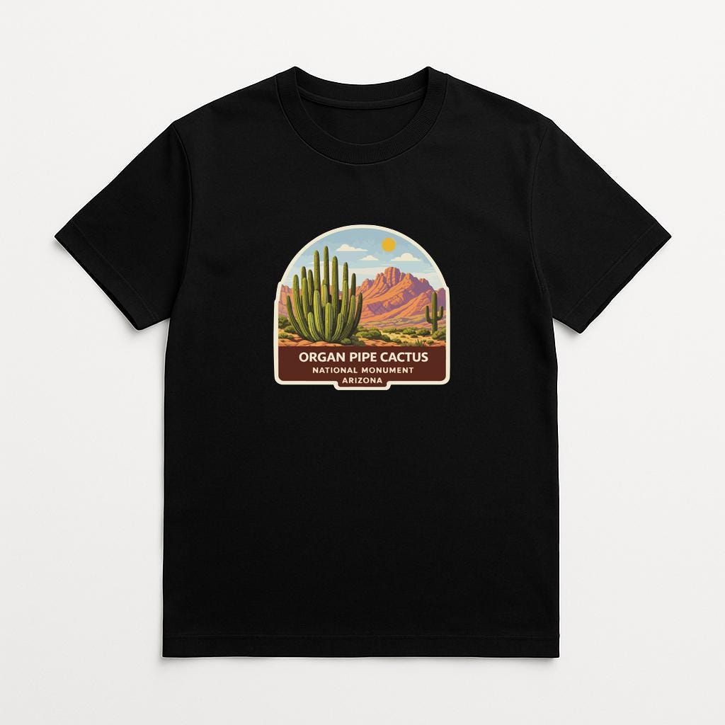 A black t-shirt with a graphic design depicting a desert landscape with cacti and mountains, along with the text "ORGAN PIPE CACTUS NATIONAL PARK ARIZONA".