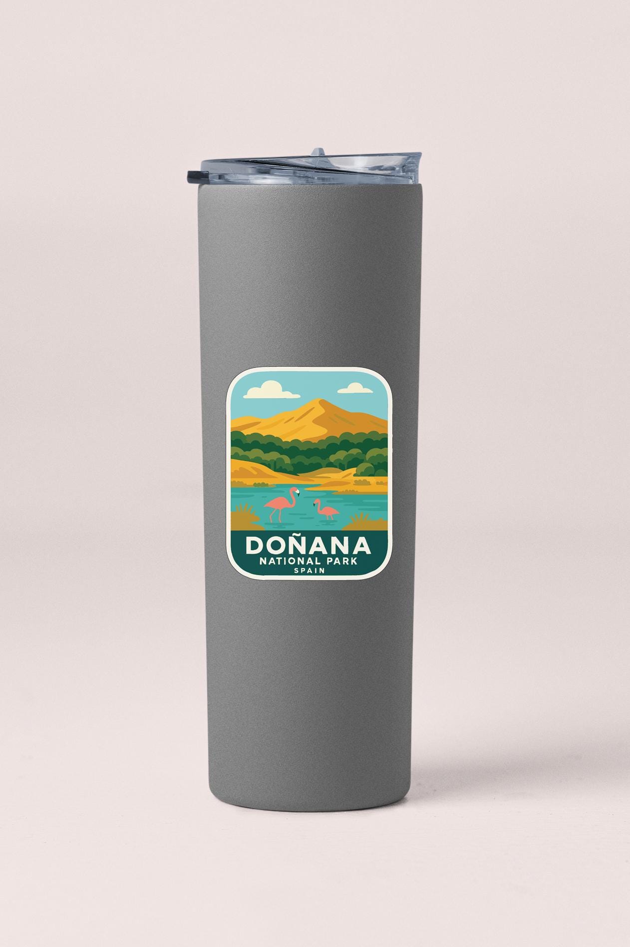 A gray insulated tumbler with a label that features an illustration of Donana National Park, including a lake, mountains, and wildlife.