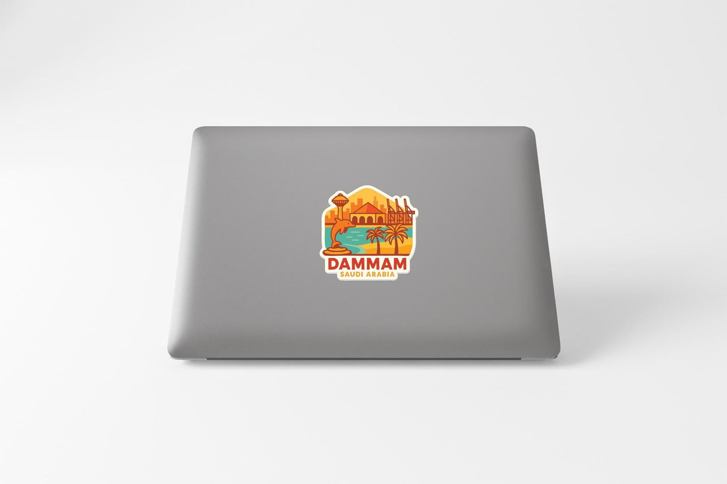 a sticker on the back of a laptop with a colorful illustration of a desert landscape and the text "DAMHAM" and "SUDAN ARABIA".