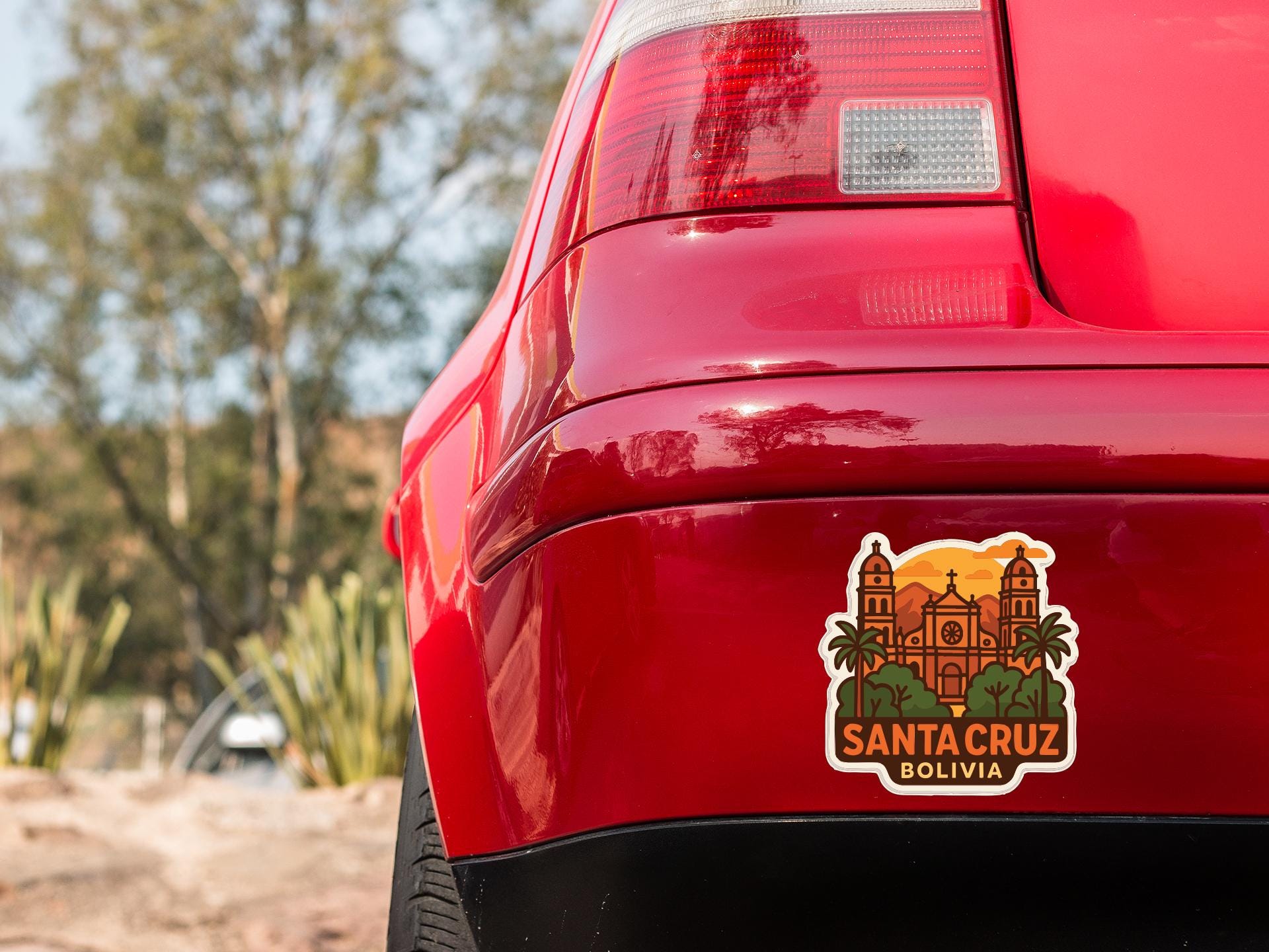 the rear end of a red car with a sticker on the trunk that features a graphic of Santa Cruz, Bolivia.