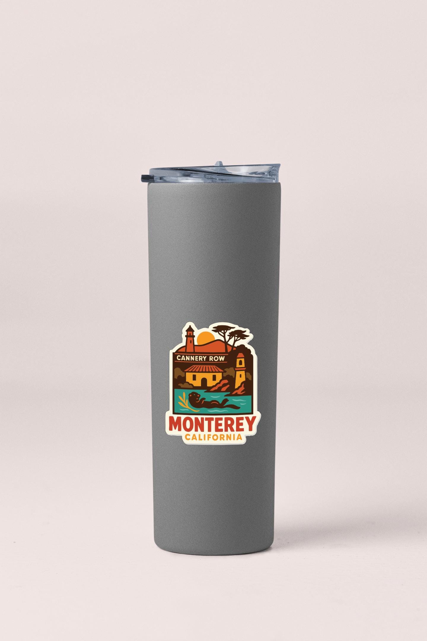 A gray insulated tumbler with a label that says "MONTEREY CALIFORNIA" and features a colorful illustration of landmarks and scenery.