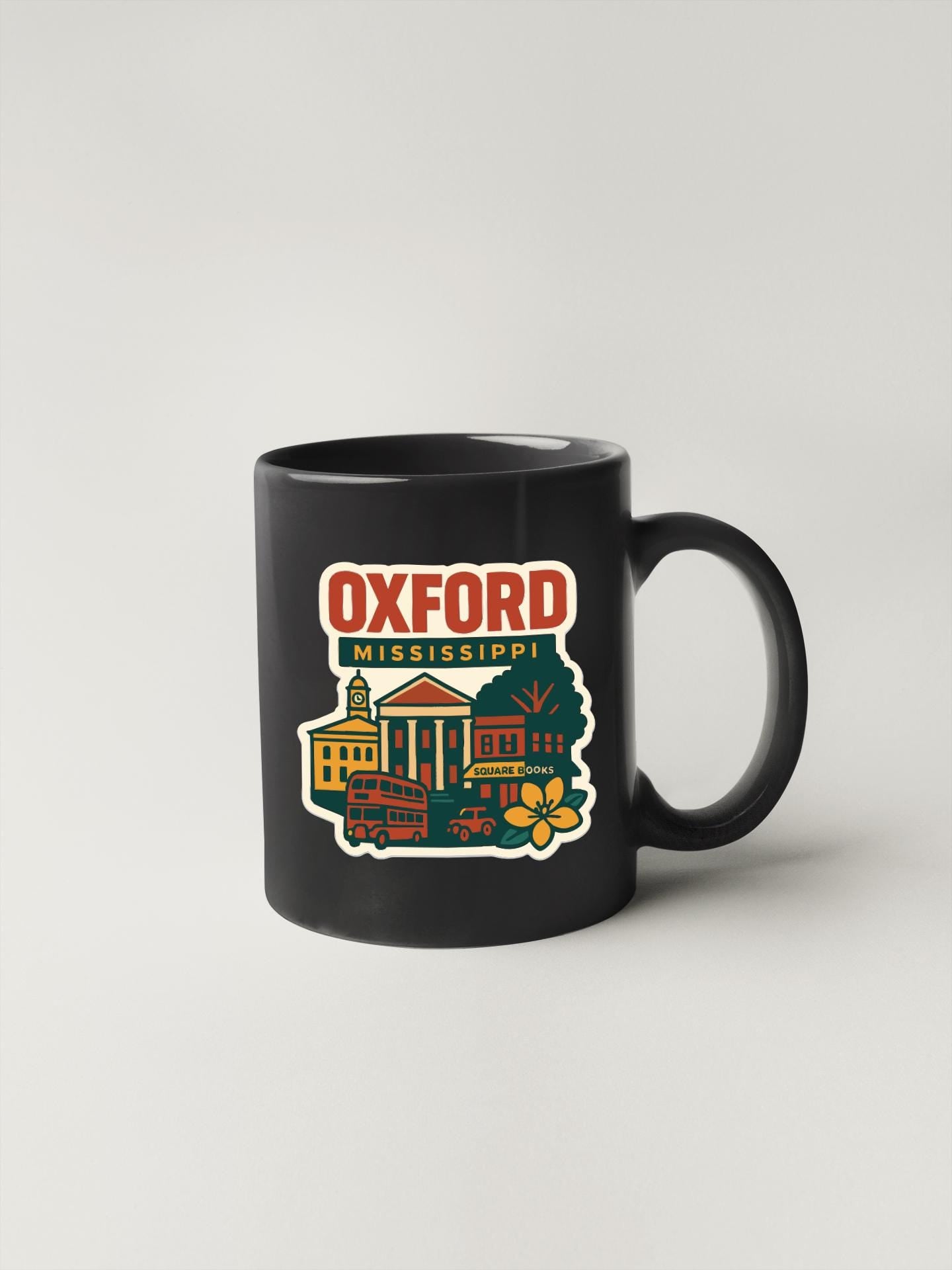 A black coffee mug with a colorful illustration of a town or city, along with the text "Oxford Mississippi" printed on it.