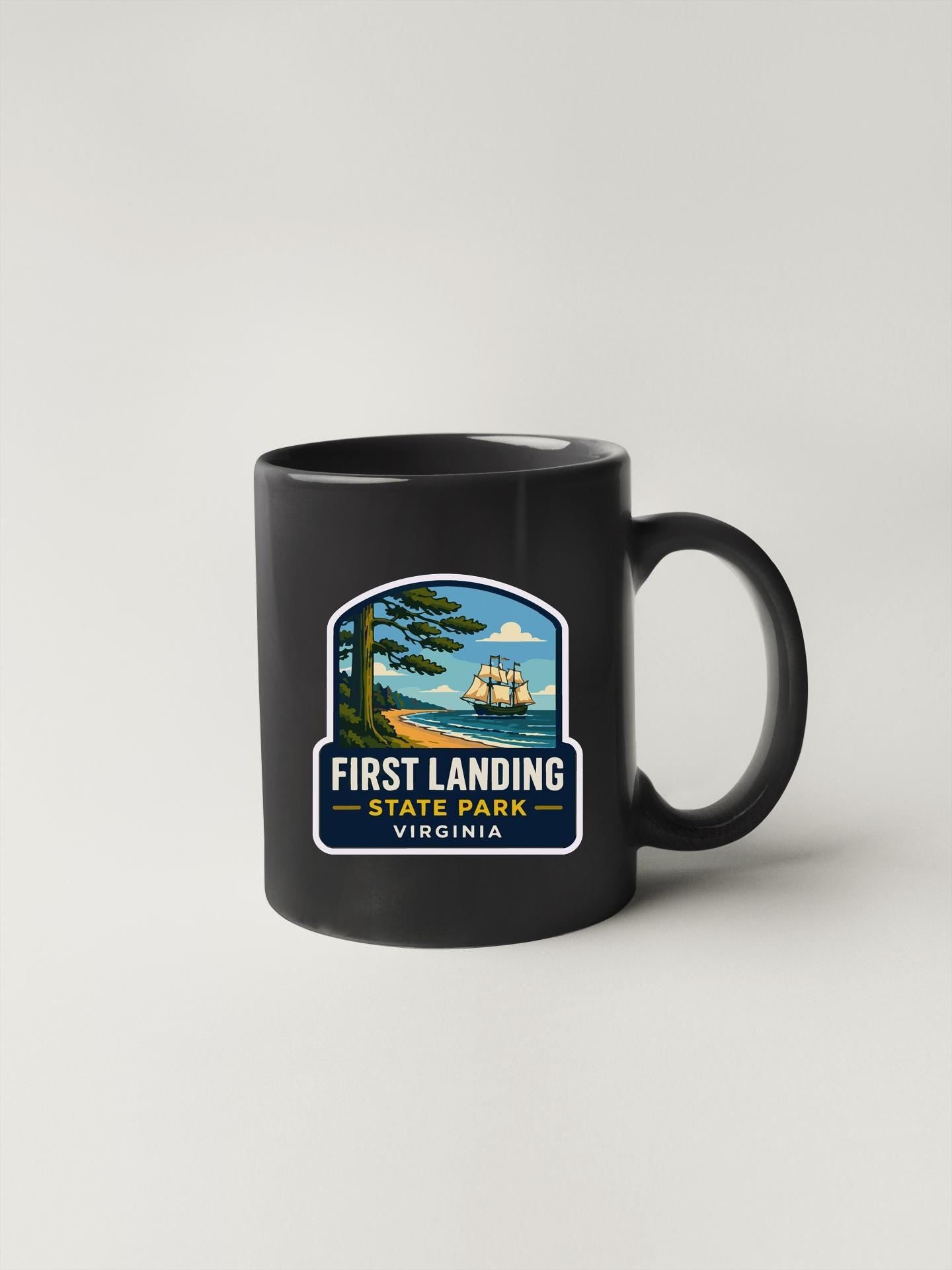 A black coffee mug with a graphic design depicting a ship sailing on a body of water, surrounded by trees and a beach.