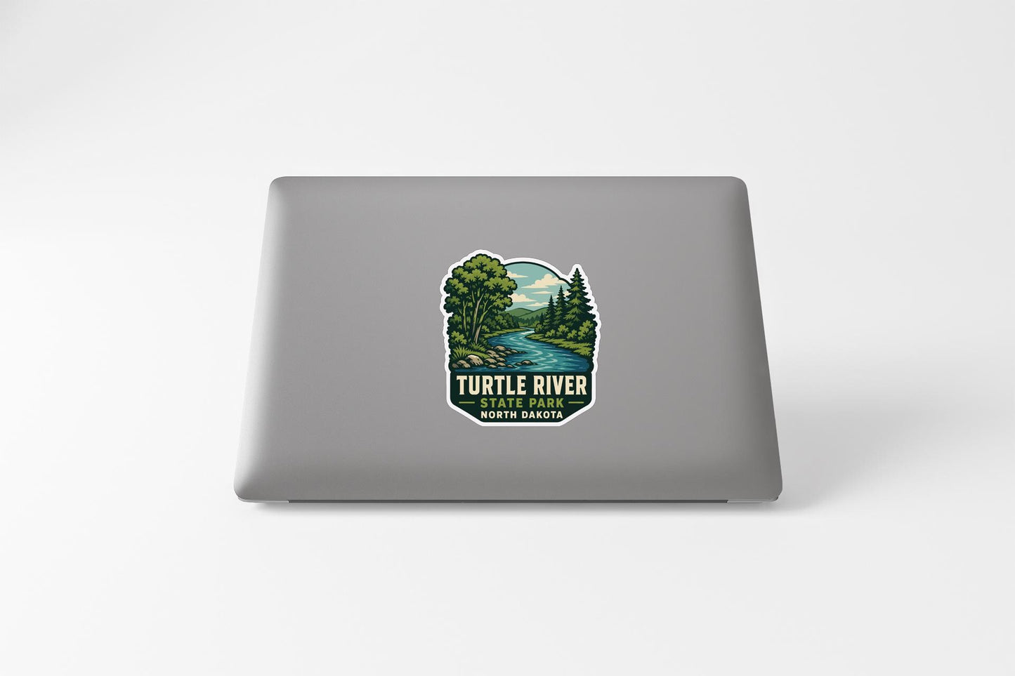 A sticker on the back of a laptop, depicting a scenic landscape with a river and trees.