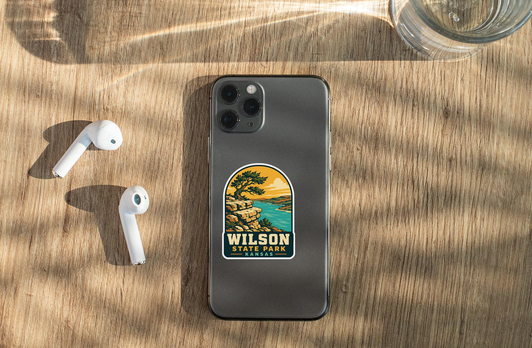 a smartphone with a sticker on the back, placed on a wooden surface alongside a pair of white earbuds and a glass of water.