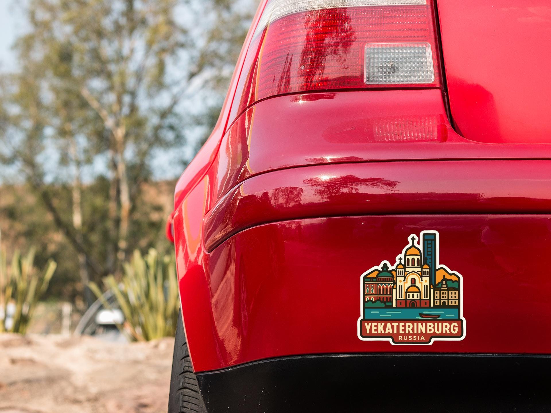 the rear end of a red car with a sticker on the trunk that features a cityscape and the text "Yekaterinburg Russia".