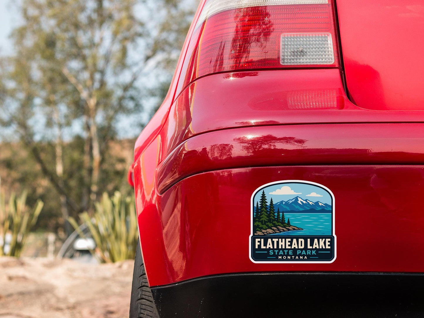 the rear end of a red car with a license plate sticker on the back window, featuring a scenic mountain landscape.