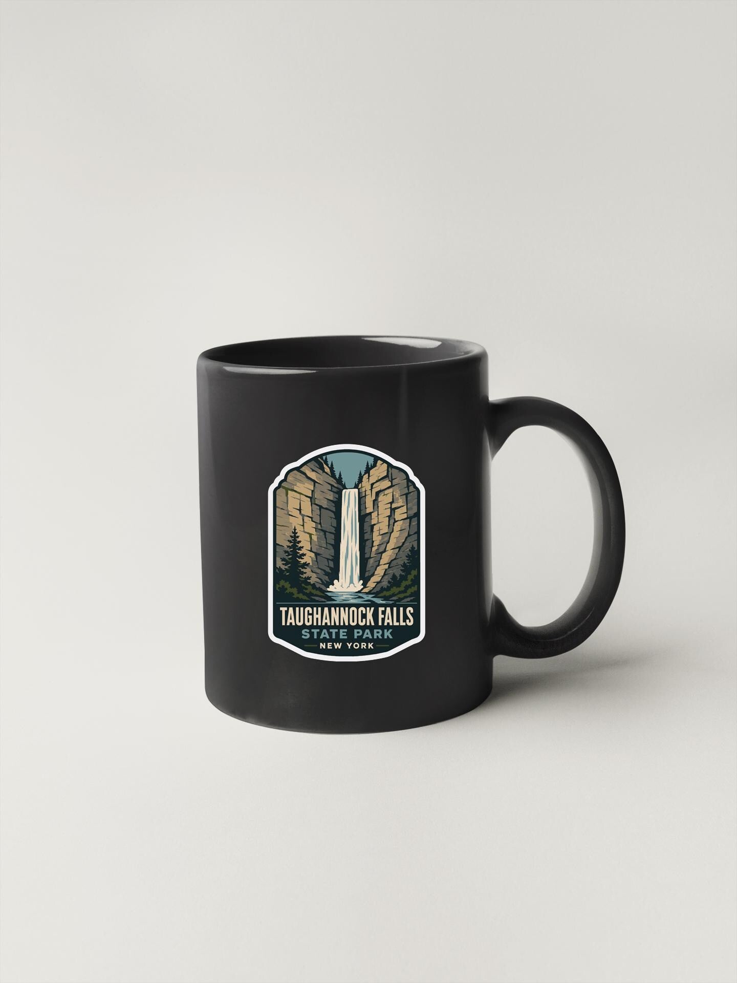 A black coffee mug with a graphic design featuring a waterfall and the text "Taughanock Falls State Park, New York".