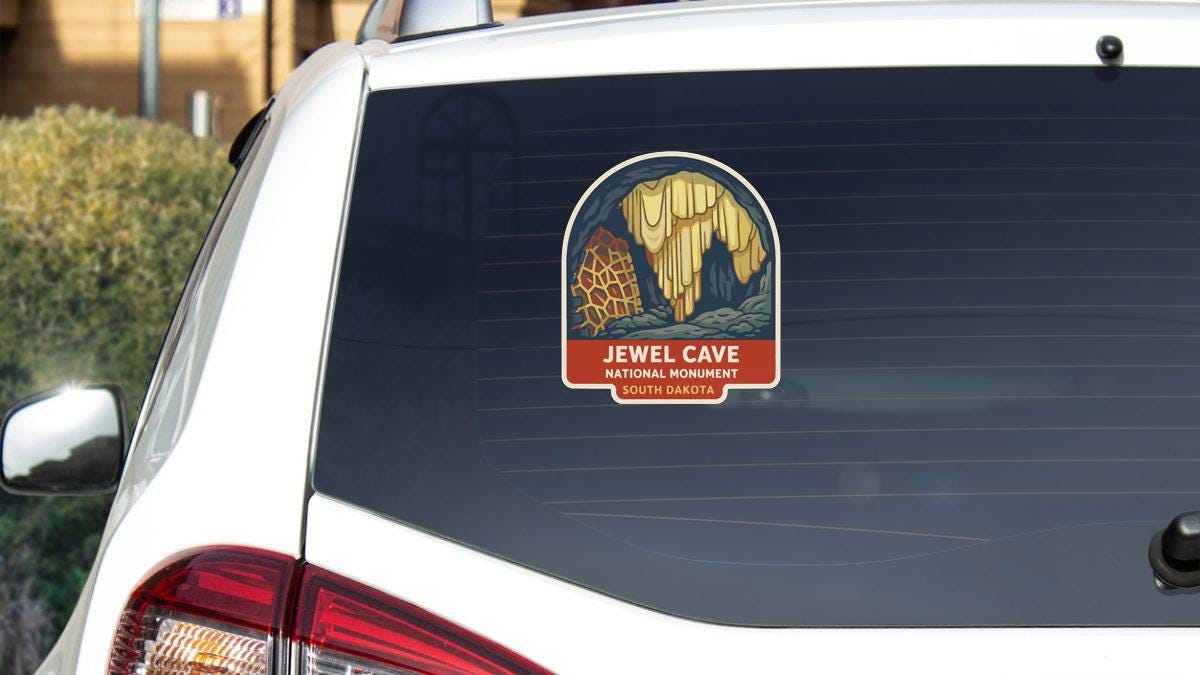 a sticker on the rear window of a white car, depicting a safari scene with a giraffe and a cave.